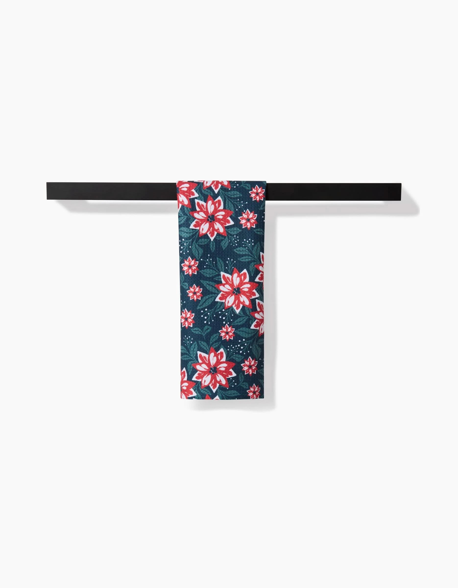 The Poinsettia Garden towel by Charlie Rowan Designs, made with Geoweave fabric and a vibrant floral pattern, hangs on a dark bar holder against a white wall.