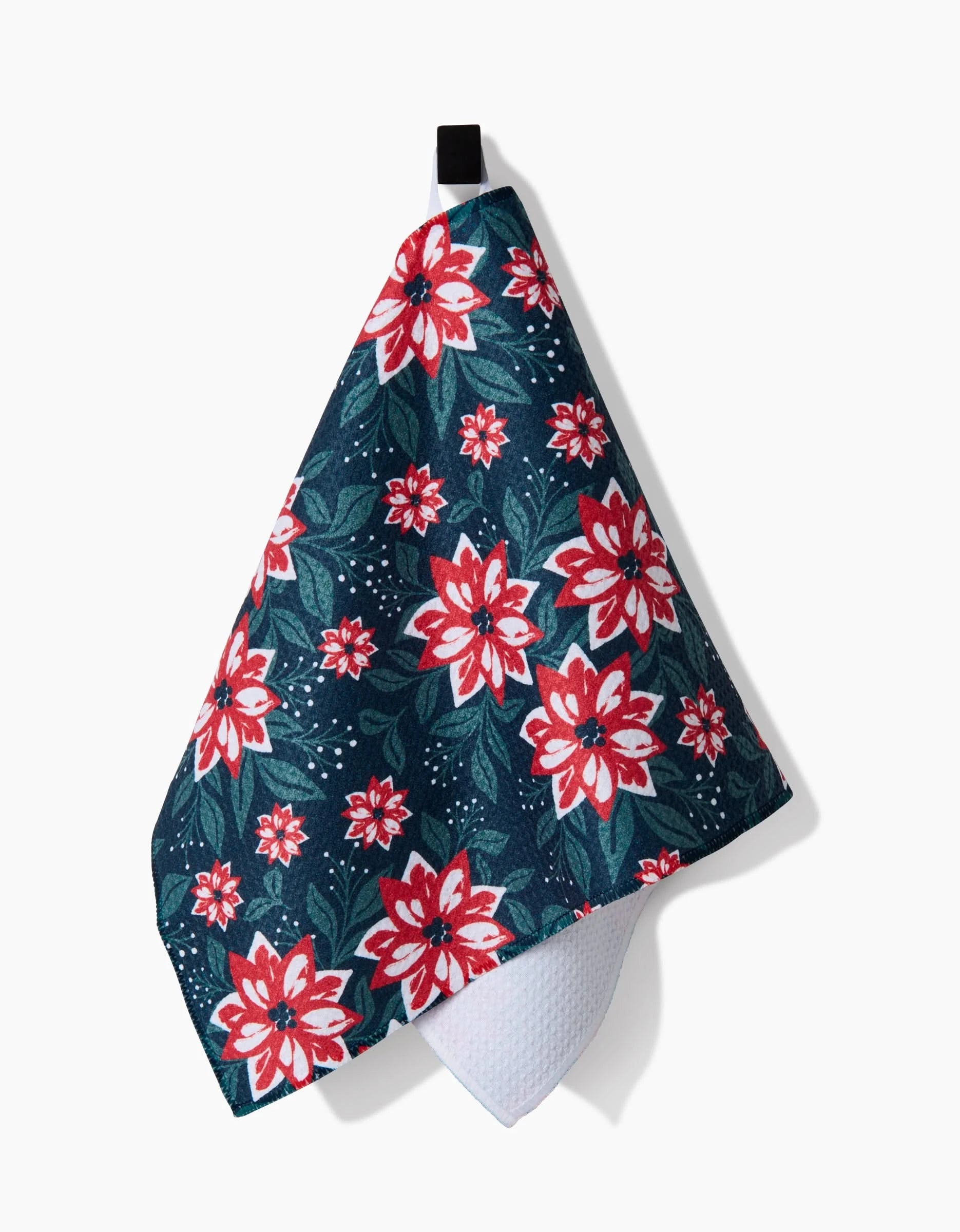 The Poinsettia Garden Bar Towel by Charlie Rowan Designs, featuring a red and white floral pattern on dark blue Geoweave fabric, hangs from a black loop against a white background.