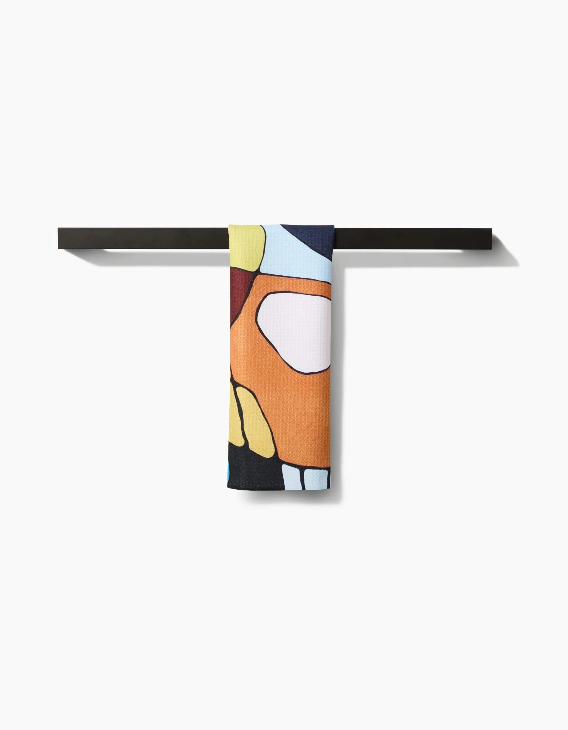 The Poppies on Blue bar towel by Rachel Austin, featuring an abstract pattern and crafted from recycled materials, hangs neatly over a minimalist black towel bar against a plain white background.