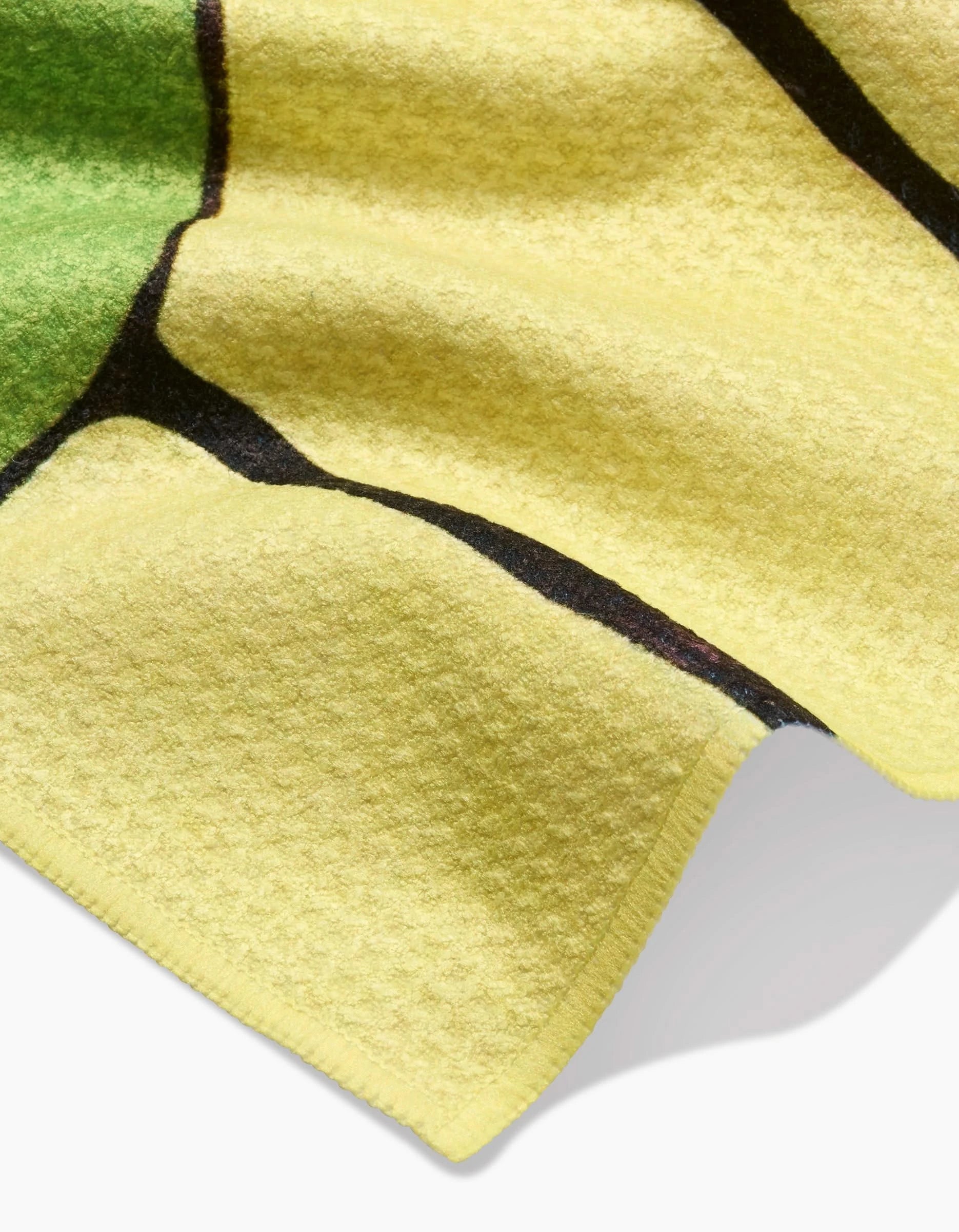 Close-up of Rachel Austin’s Poppies on Yellow Bar Towel, featuring soft yellow Geoweave fabric with a green and black pattern, as the towel’s edge gently lifts from a flat surface.