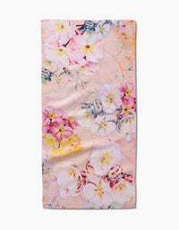 The Primroses bar towel by Pascale Dilger features a pastel pink background adorned with scattered pink, yellow, blue, and white florals. Made from soft Geoweave fabric, it offers an elegant and delicate design.