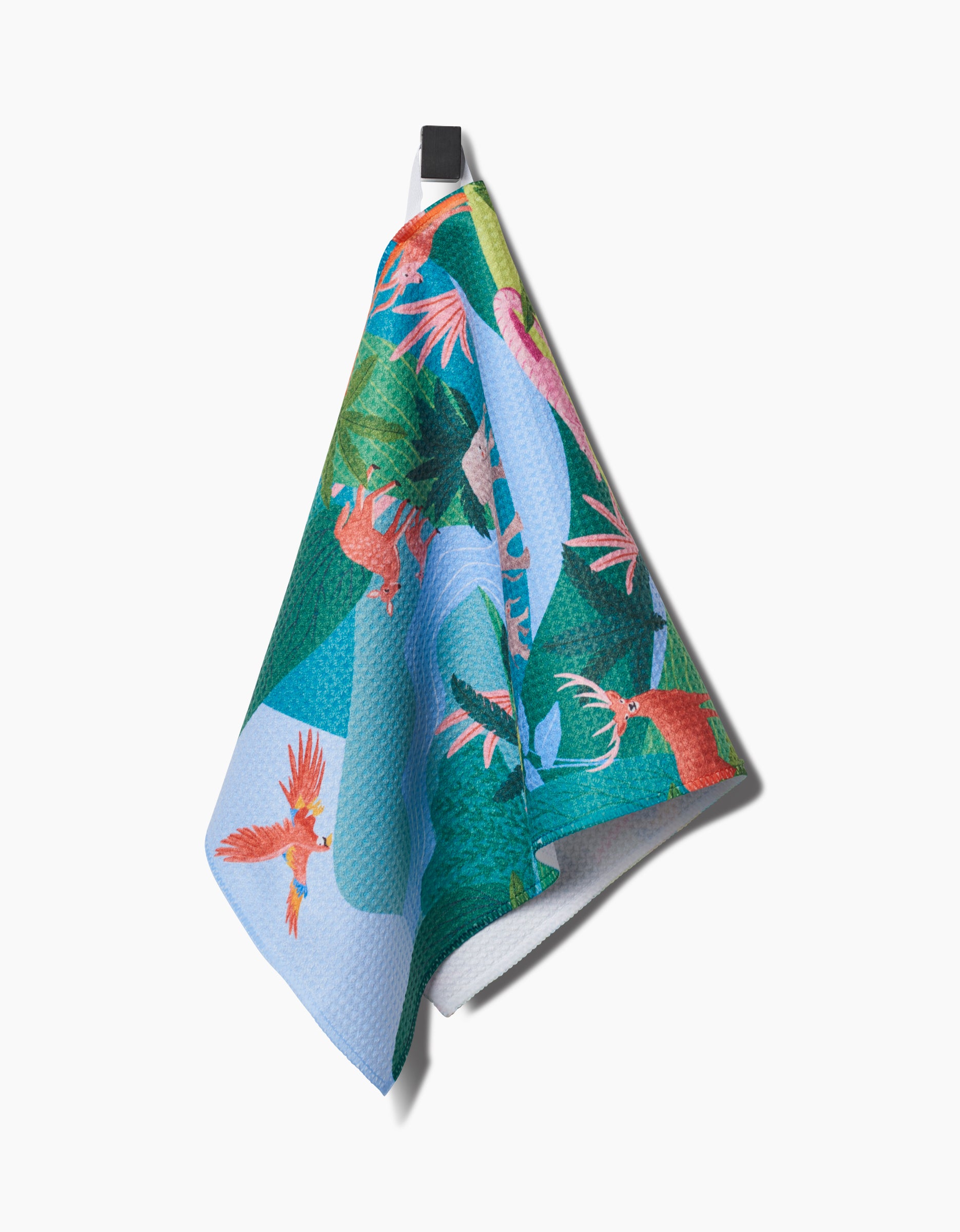The Rainforest bar towel by Ceyda Alasar features vibrant parrots and green foliage, crafted from recycled materials. It hangs from a black hook against a white background.