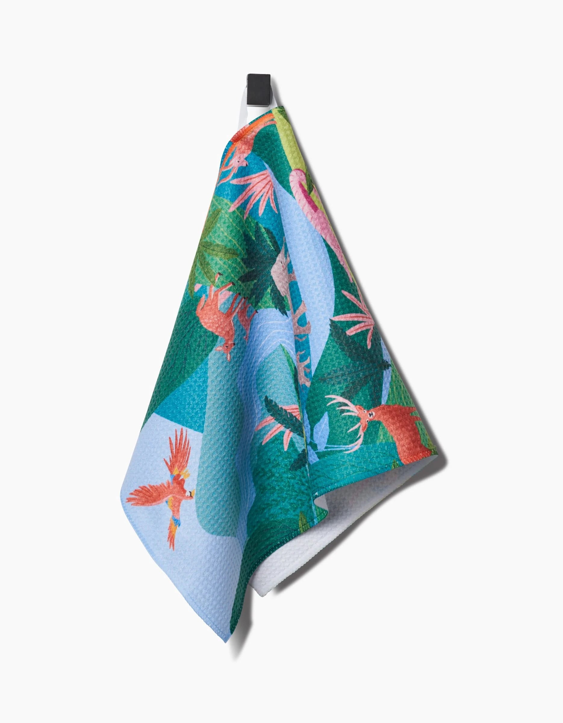 The Rainforest bar towel by Ceyda Alasar features vibrant parrots and green foliage, crafted from recycled materials. It hangs from a black hook against a white background.