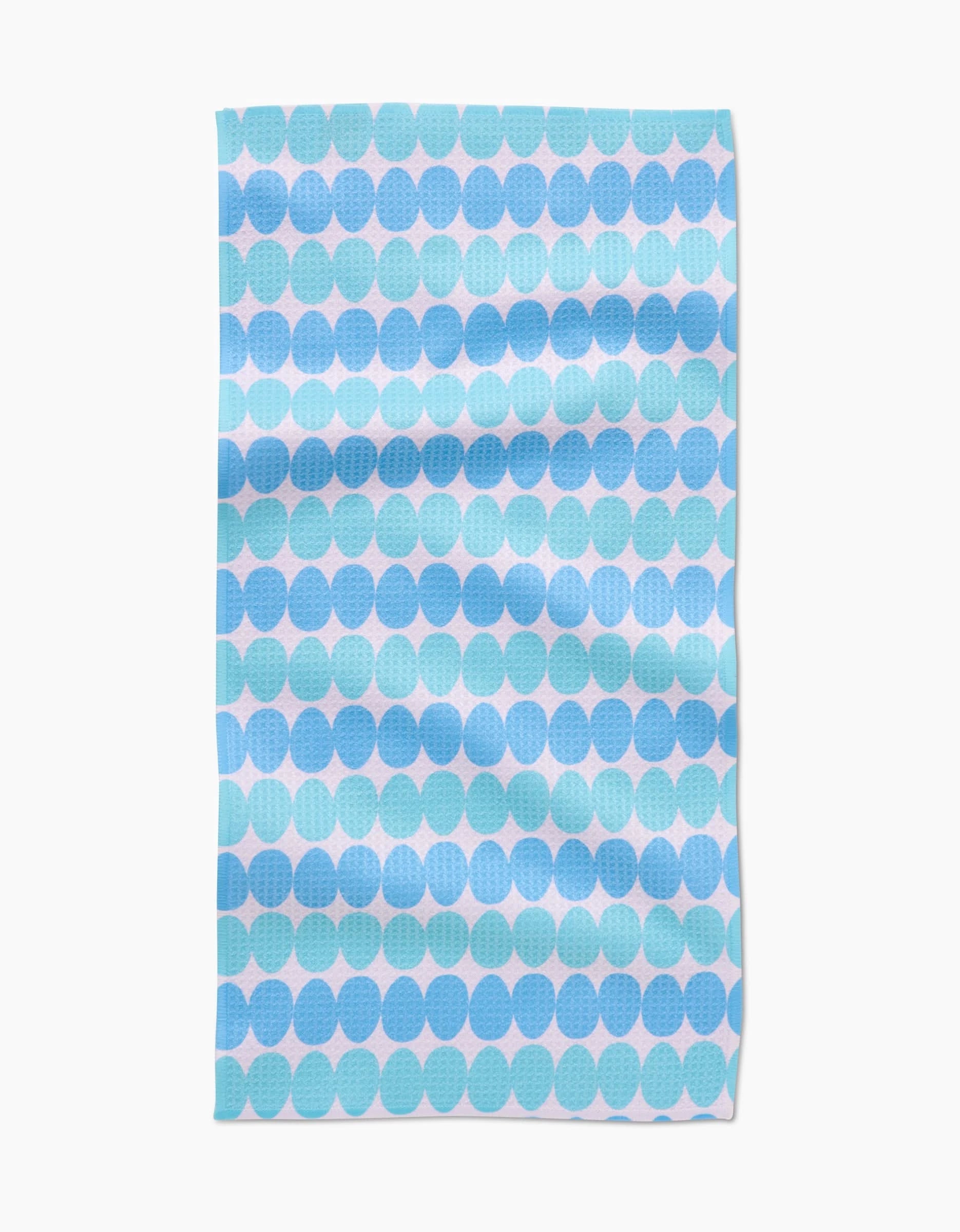 The Kayla Ann Robins Egg Bar Towel features a blue and light blue circle pattern on white Geoweave fabric. With visible folds and a slightly textured surface, it combines style with durability.