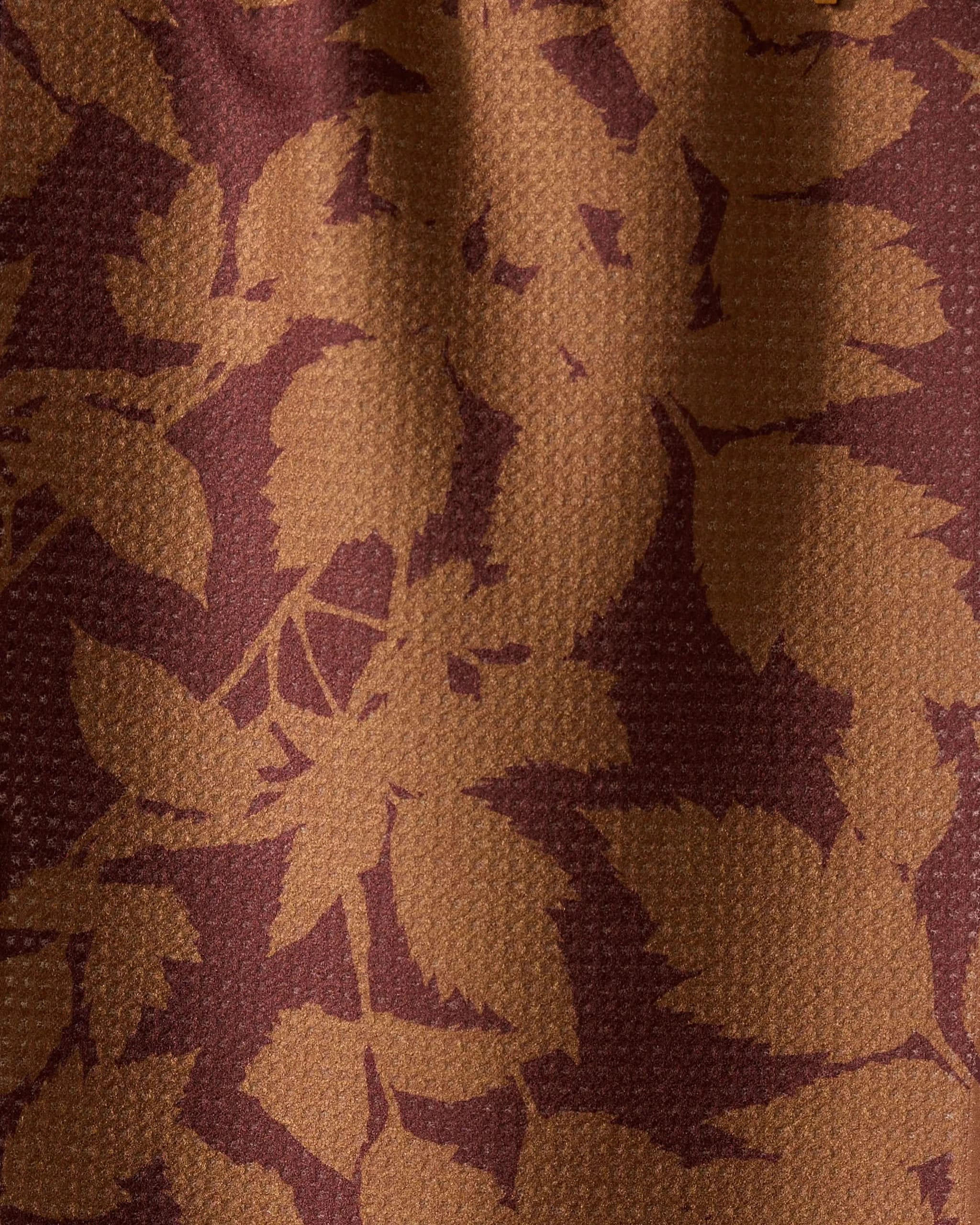 The Geometry Rustle towel features a close-up of textured fabric with overlapping leafy patterns in brown and maroon, highlighting its ultra-absorbent quality—perfect for everyday use.