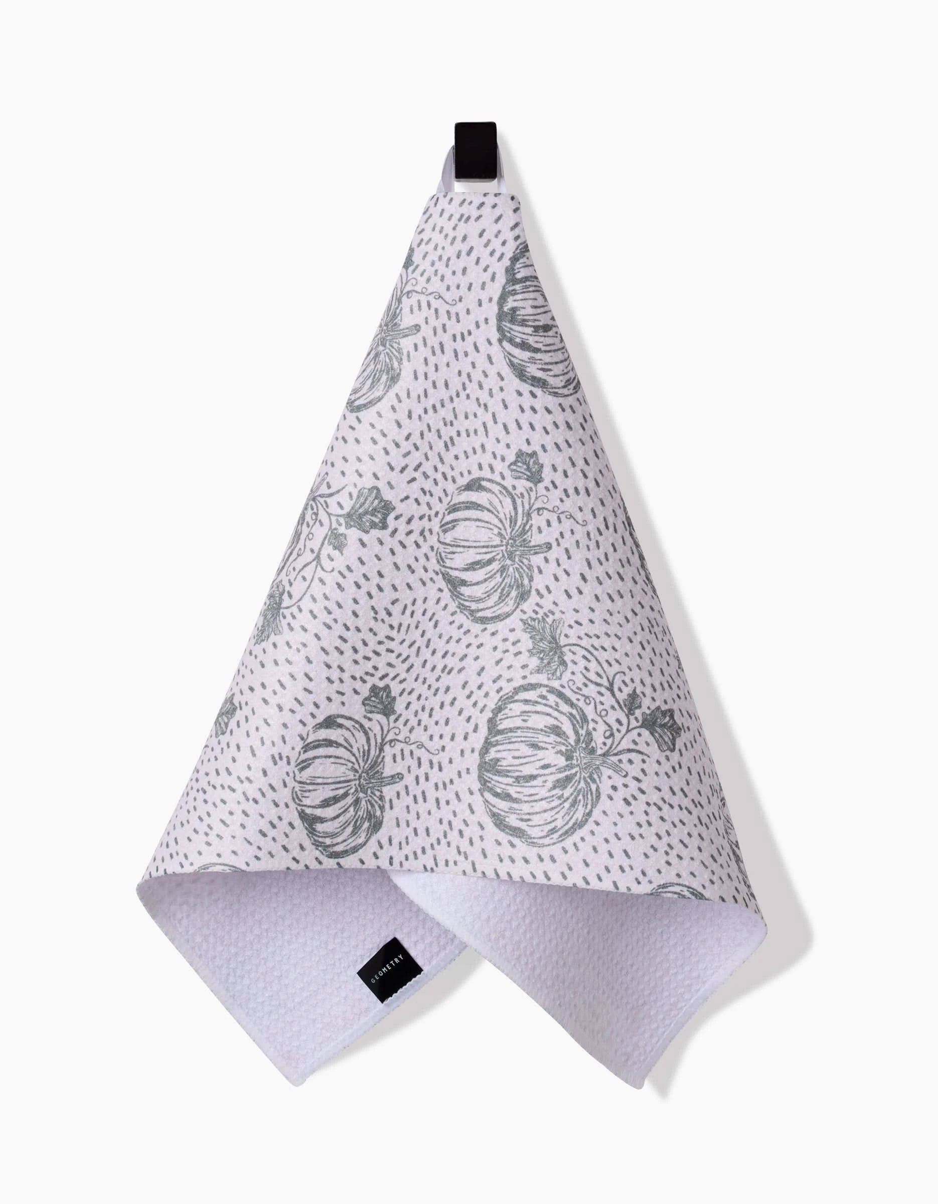 The Sage Pumpkin Field Bar Towel by Charlie Rowan Designs, crafted from Geoweave fabric, features gray pumpkin illustrations and dotted patterns. It hangs from a black loop against a white background.