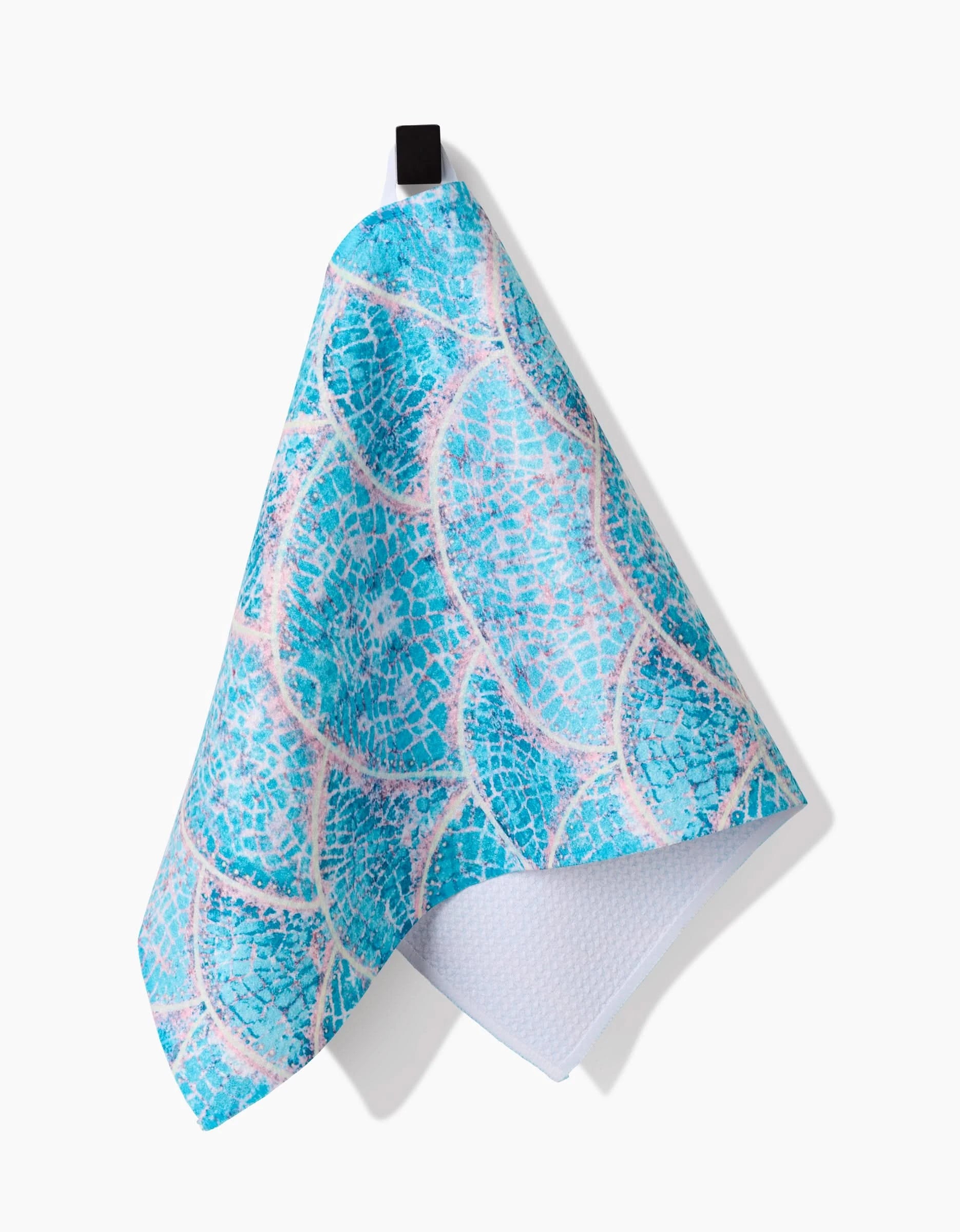 The Scallop Hills Bar Towel by Taryn Brennan features a scale-inspired turquoise and white pattern in Geoweave fabric, hanging from a black loop against a white background.