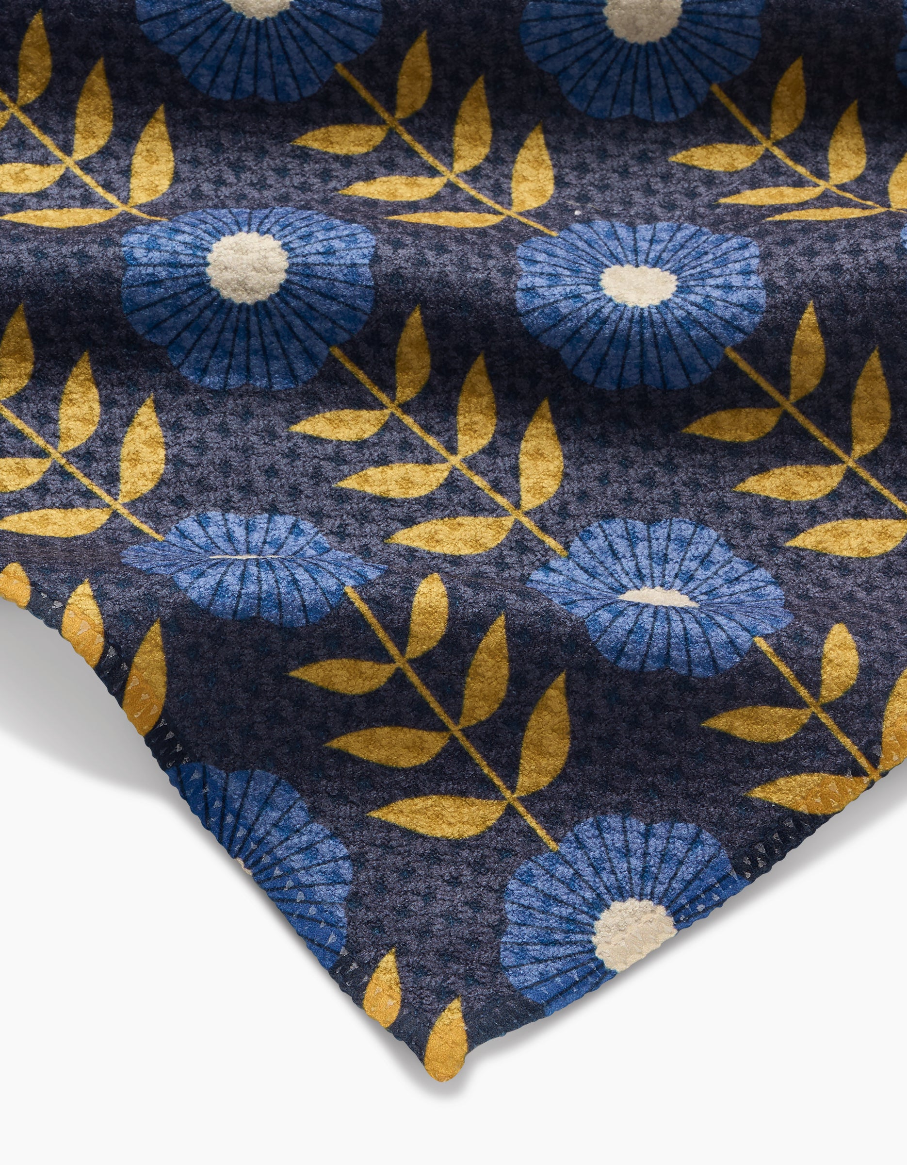 A close-up of Megan Kampa’s Scandi Floral shows eco-friendly Geoweave fabric patterned with blue flowers, white centers, and yellow leaves on a dark background. The Geoweave corner appears in the lower right.