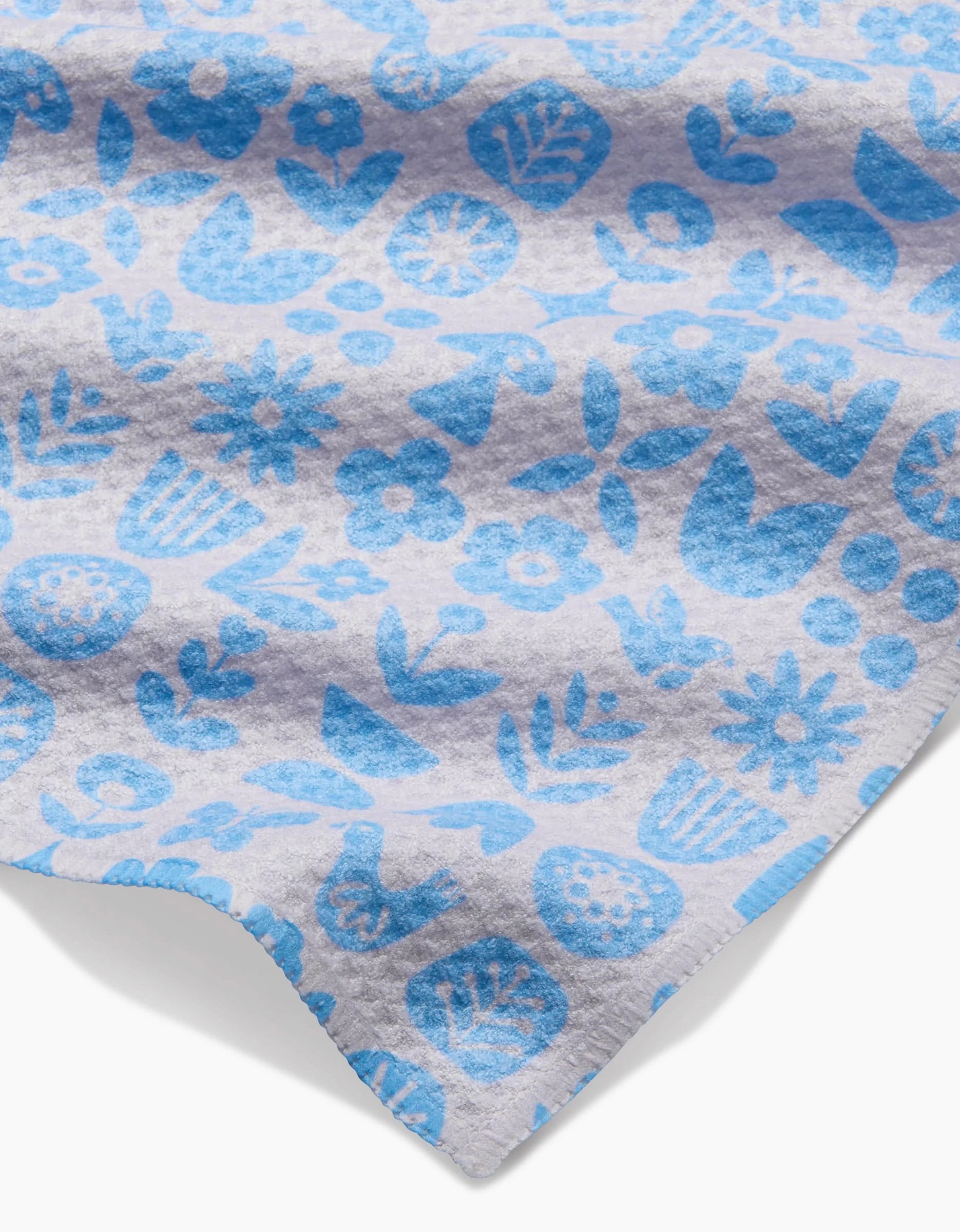 A close-up of the Kayla Ann Scandi Spring Blue bar towel shows its light gray Geoweave fabric with a blue floral and leaf pattern. Made from post-consumer recycled materials, it has a soft texture and slightly wavy edge.