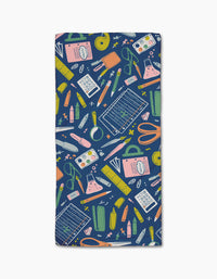 The School Days bar towel by Amy MacCready is rectangular, made from post-consumer recycled materials, and displays a vibrant school supplies pattern—rulers, scissors, calculators—on a dark blue background.