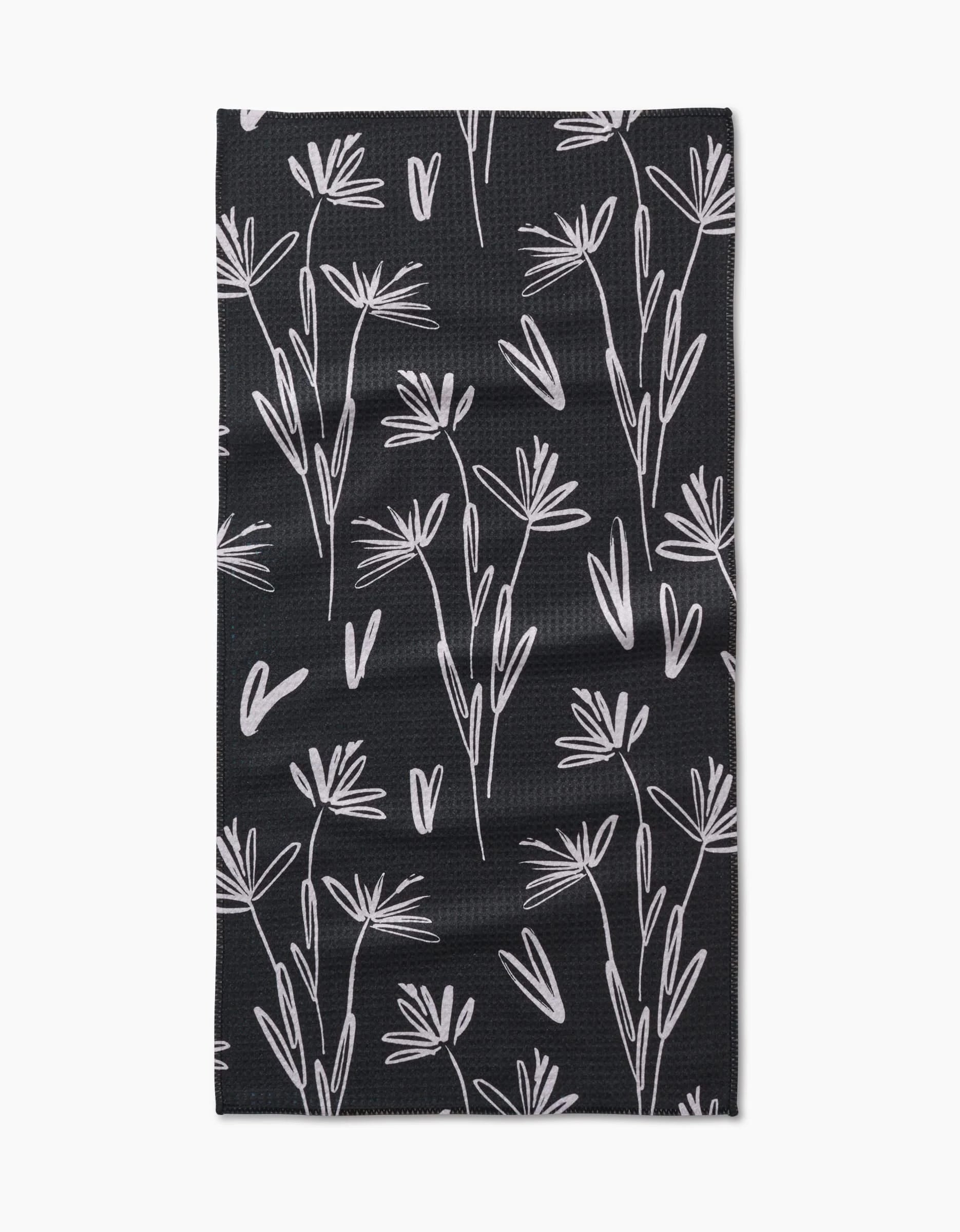The Toboggan Avenue Sketchbook Dust bar towel is black, rectangular, and made from Geoweave fabric. It features a white minimalist botanical pattern with delicate, abstract flower and leaf outlines across the surface.