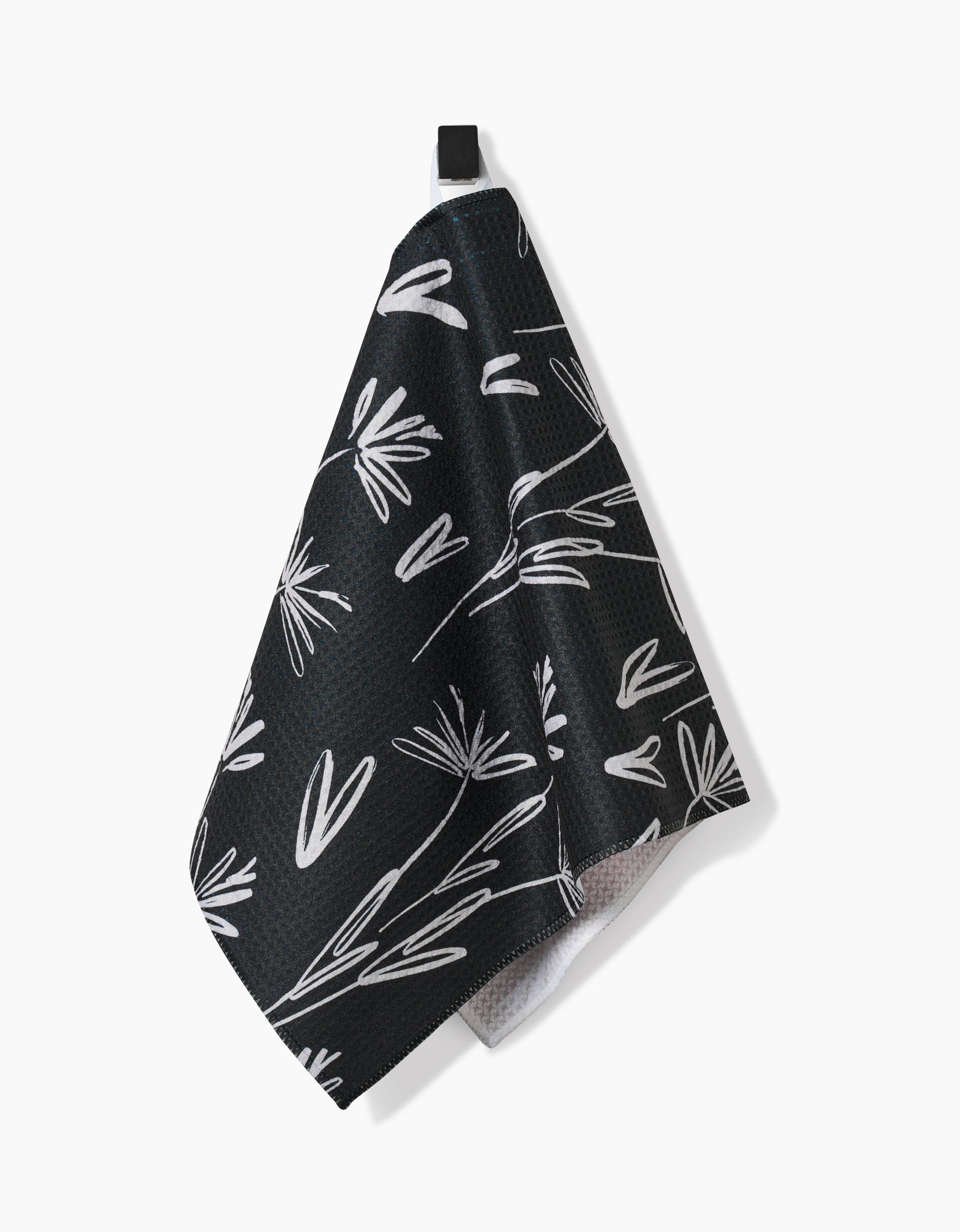 The Sketchbook Dust Bar Towel by Toboggan Avenue features a black background with a white botanical leaf and stem pattern, crafted from recycled materials, and hangs from a small black loop against a white backdrop.