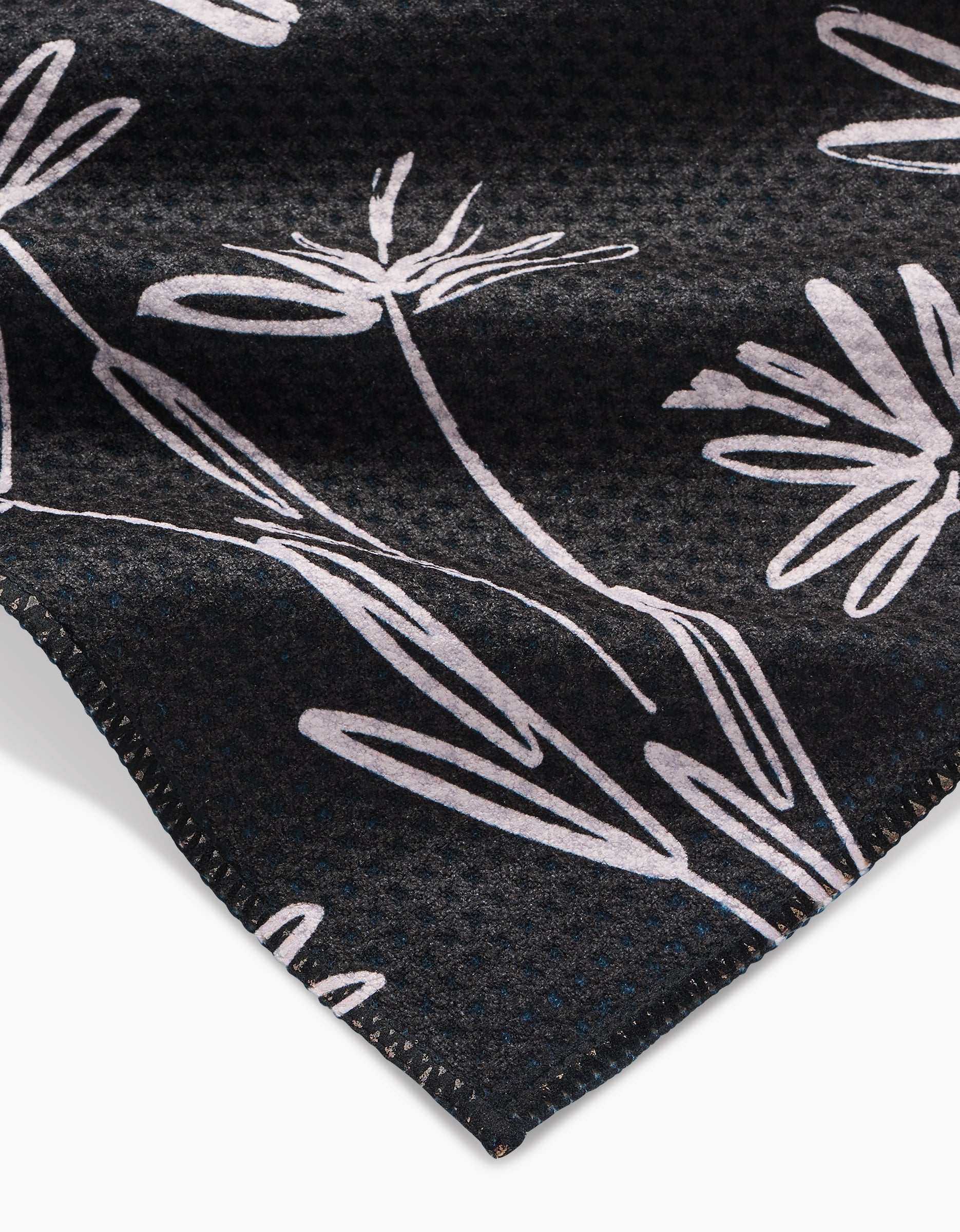 Close-up of Toboggan Avenues Sketchbook Dust: a dark Geoweave bar towel with a subtle textured pattern, white abstract floral line drawings, and neatly stitched edges.
