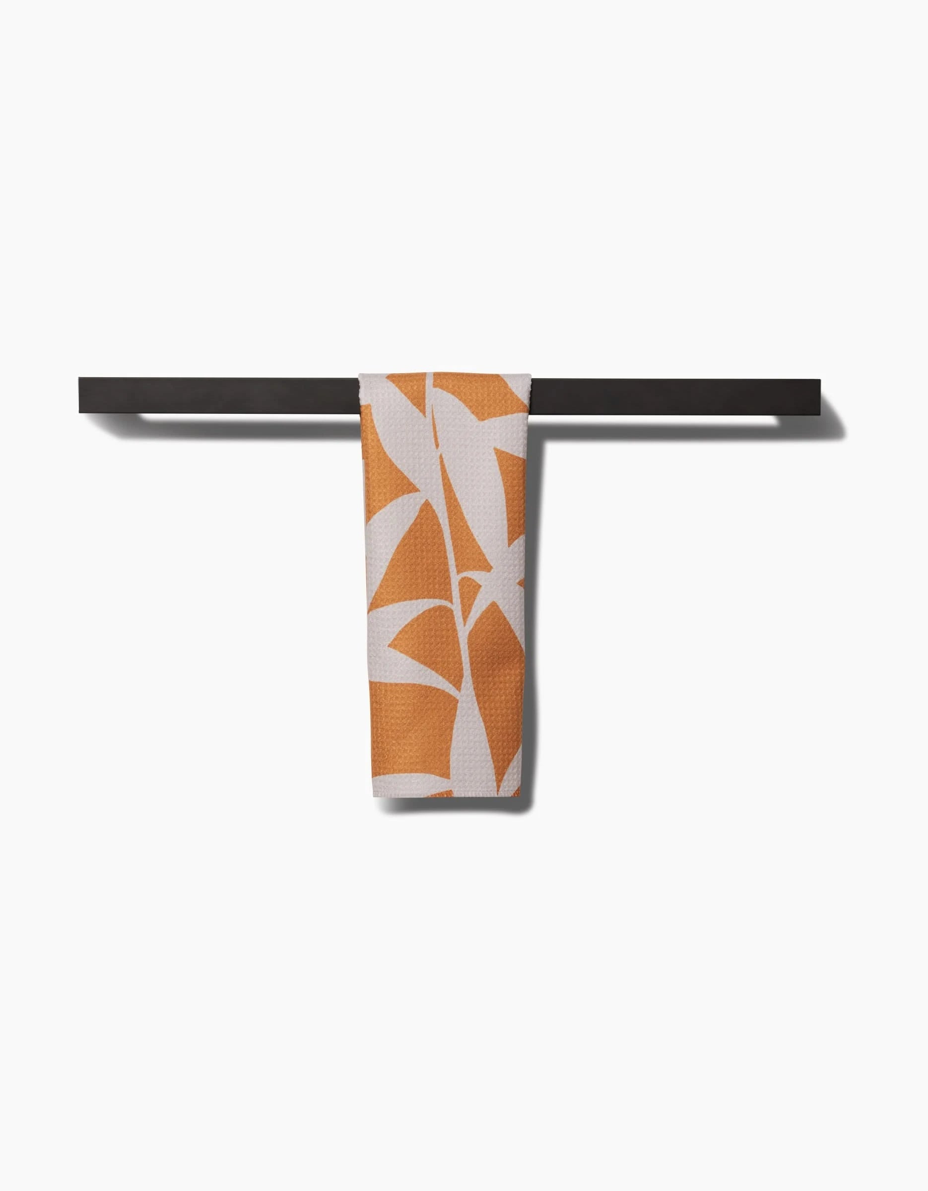 The PrintedPlant Solidago bar towel, crafted from recycled materials with an orange abstract leaf pattern, is neatly draped over a black horizontal towel bar against a plain white background.