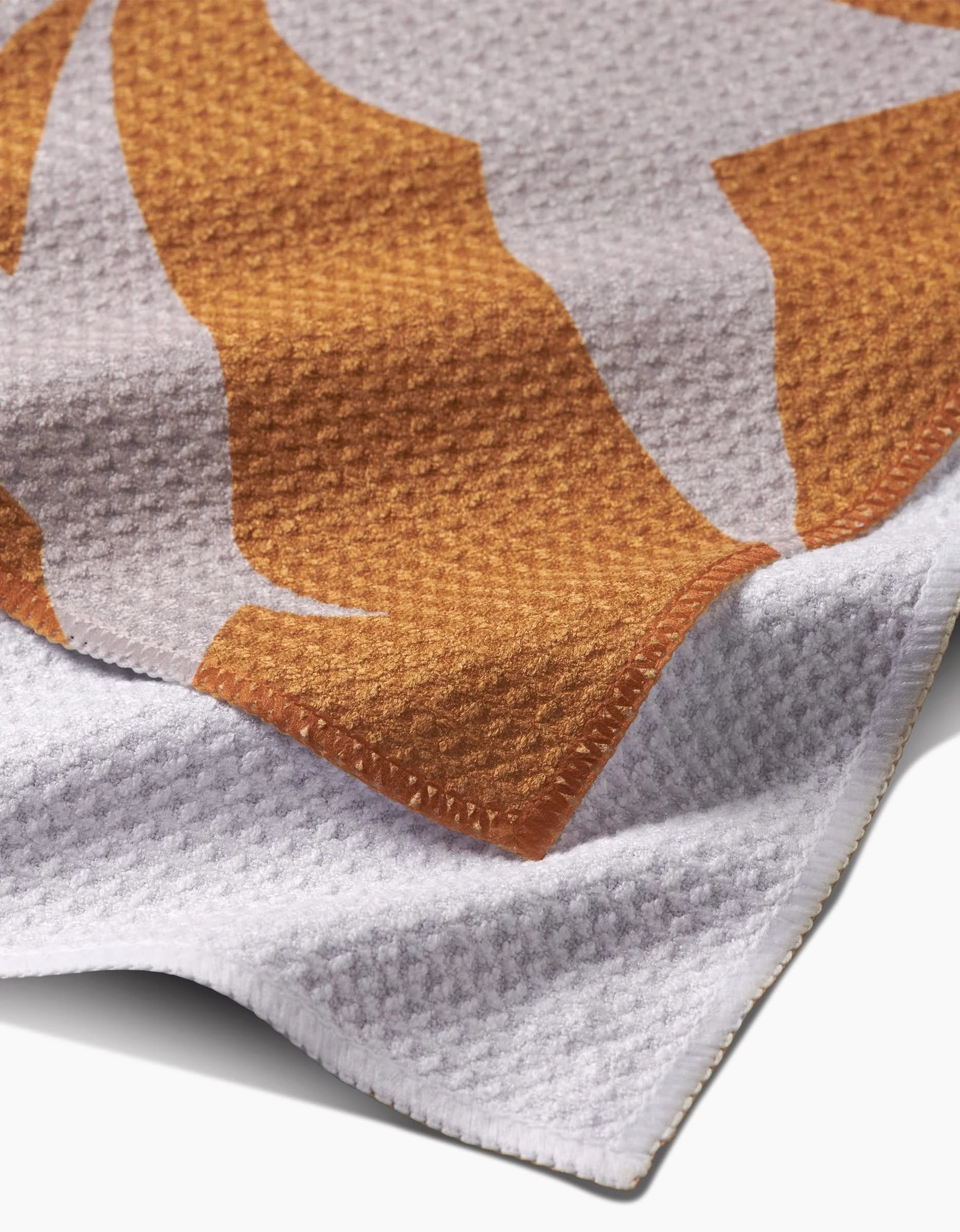 A close-up of PrintedPlants Solidago bar towel shows its textured Geoweave fabric, white base, and bold orange and beige abstract pattern, highlighting the woven detail and folded edges.