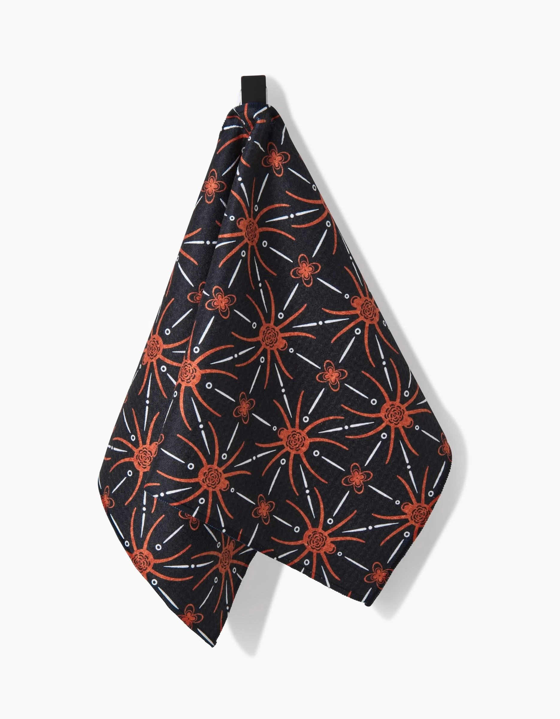 The Spider Geometric kitchen towel by Sarah Daugherty, made from recycled material, features bold orange, white, and red abstract flower patterns and hangs from a black loop against a white background.