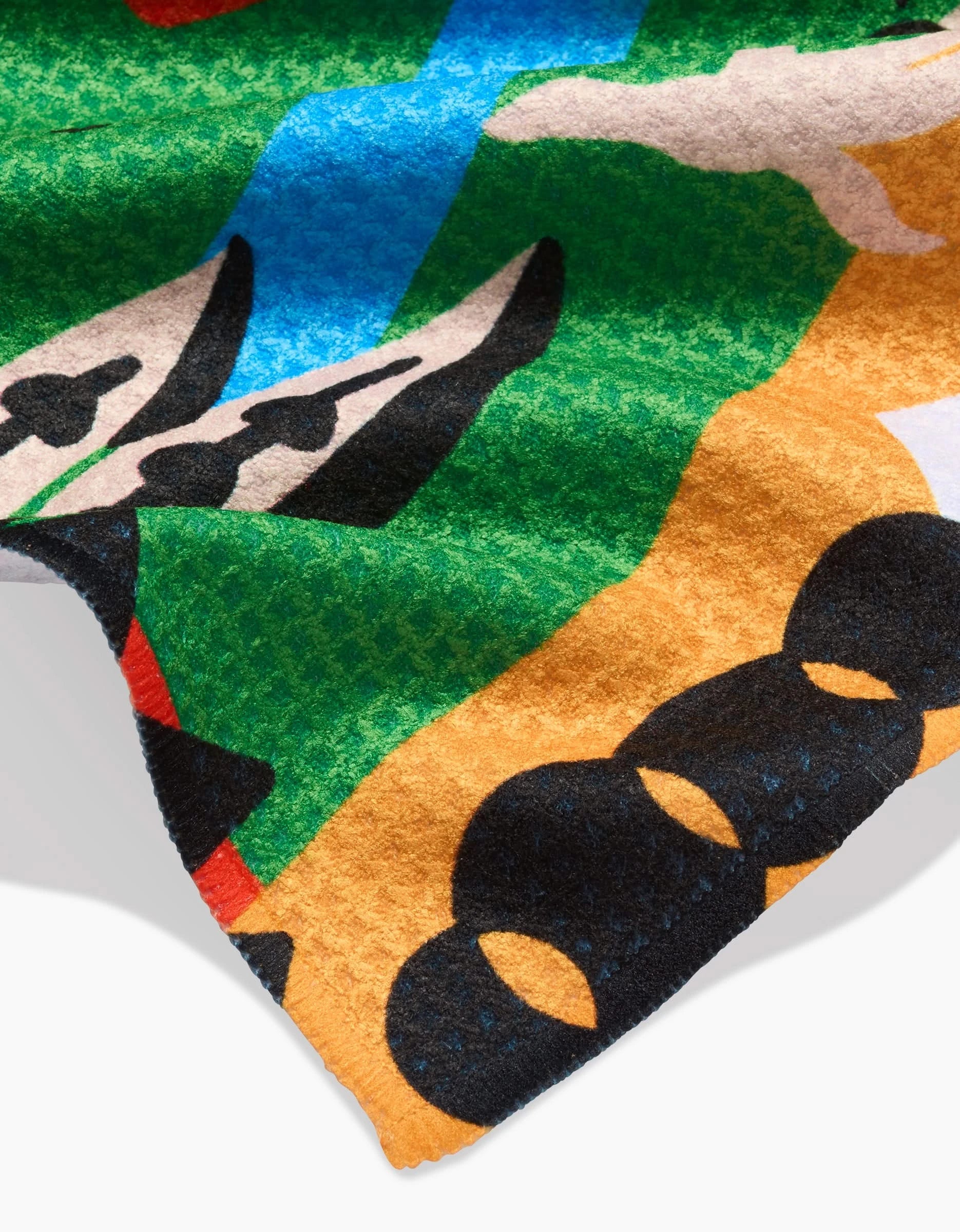 A close-up of the Tamanduá Bandeira Bar Towel by Camila Leão, showing colorful Geoweave fabric with abstract shapes—black circles, green, tan, white, and blue patterns—and the fabric’s edge visible at the lower left.