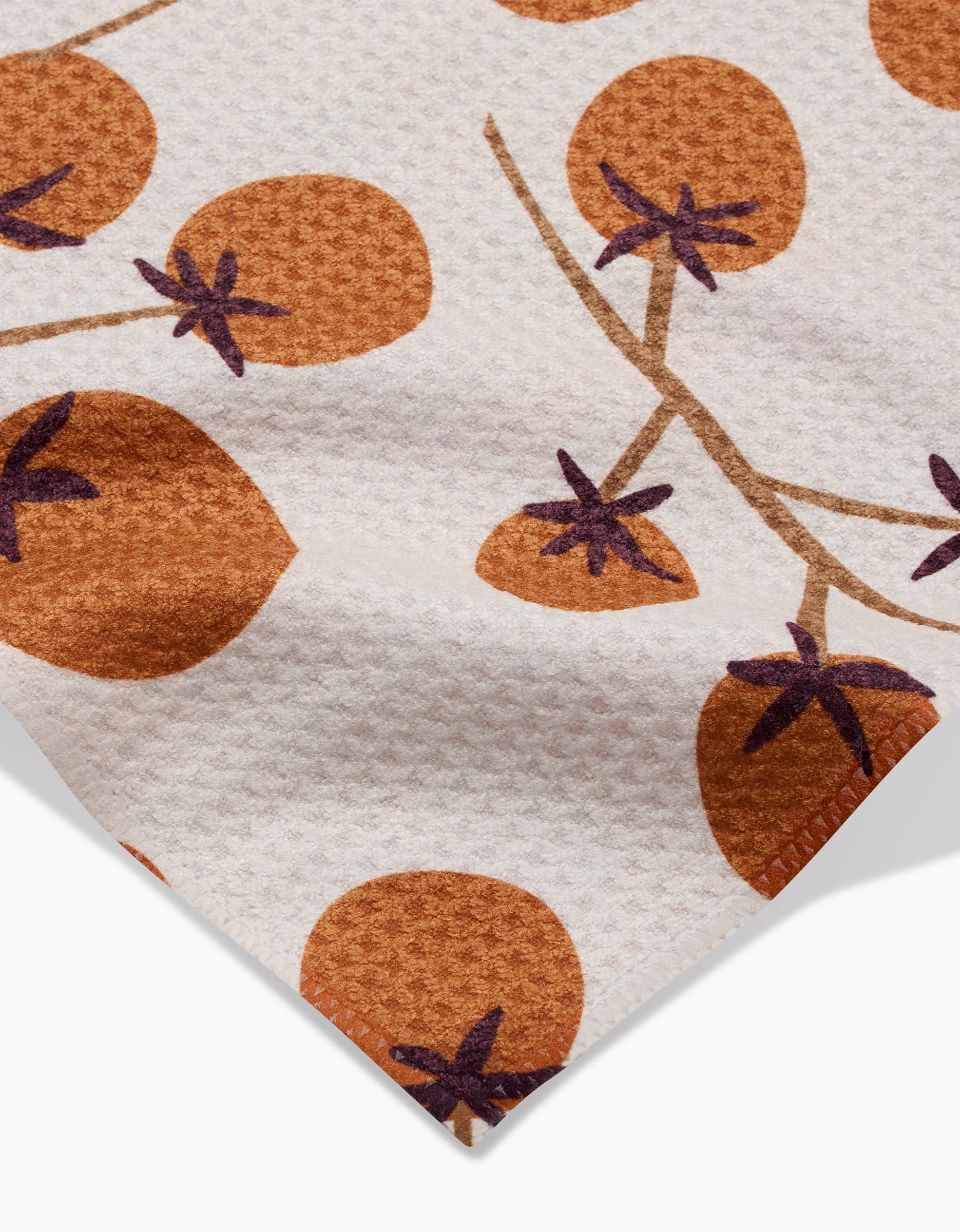 A close-up of the Lizzie Clark Tomato Harvest Bar Towel shows its white Geoweave fabric with a repeating brown tomato pattern featuring purple stems and branches. A towel corner is visible.