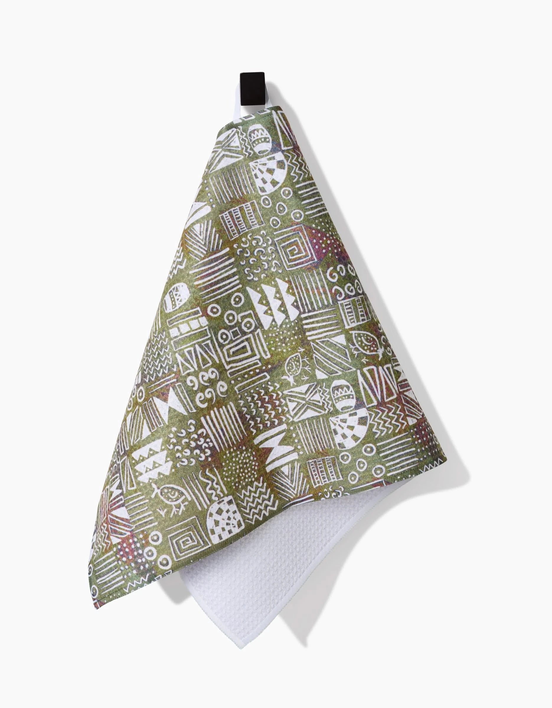 The Taryn Brennan Tribal Symbols dish towel, featuring green, white, and pink geometric patterns on eco-friendly Geoweave fabric, hangs from a black loop against a white background with a slight shadow.