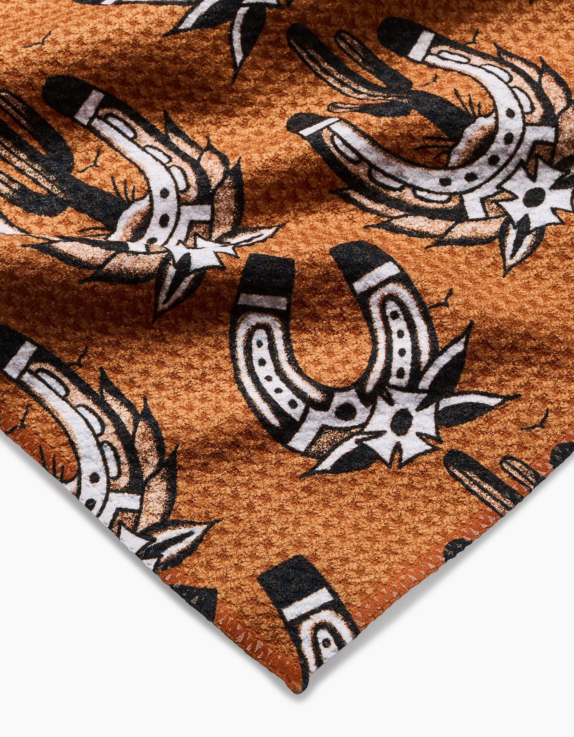 A close-up of Cole Strems Western Horseshoes bar towel, featuring textured brown Geoweave fabric with a black and white southwestern pattern of horseshoes, stars, and cacti.