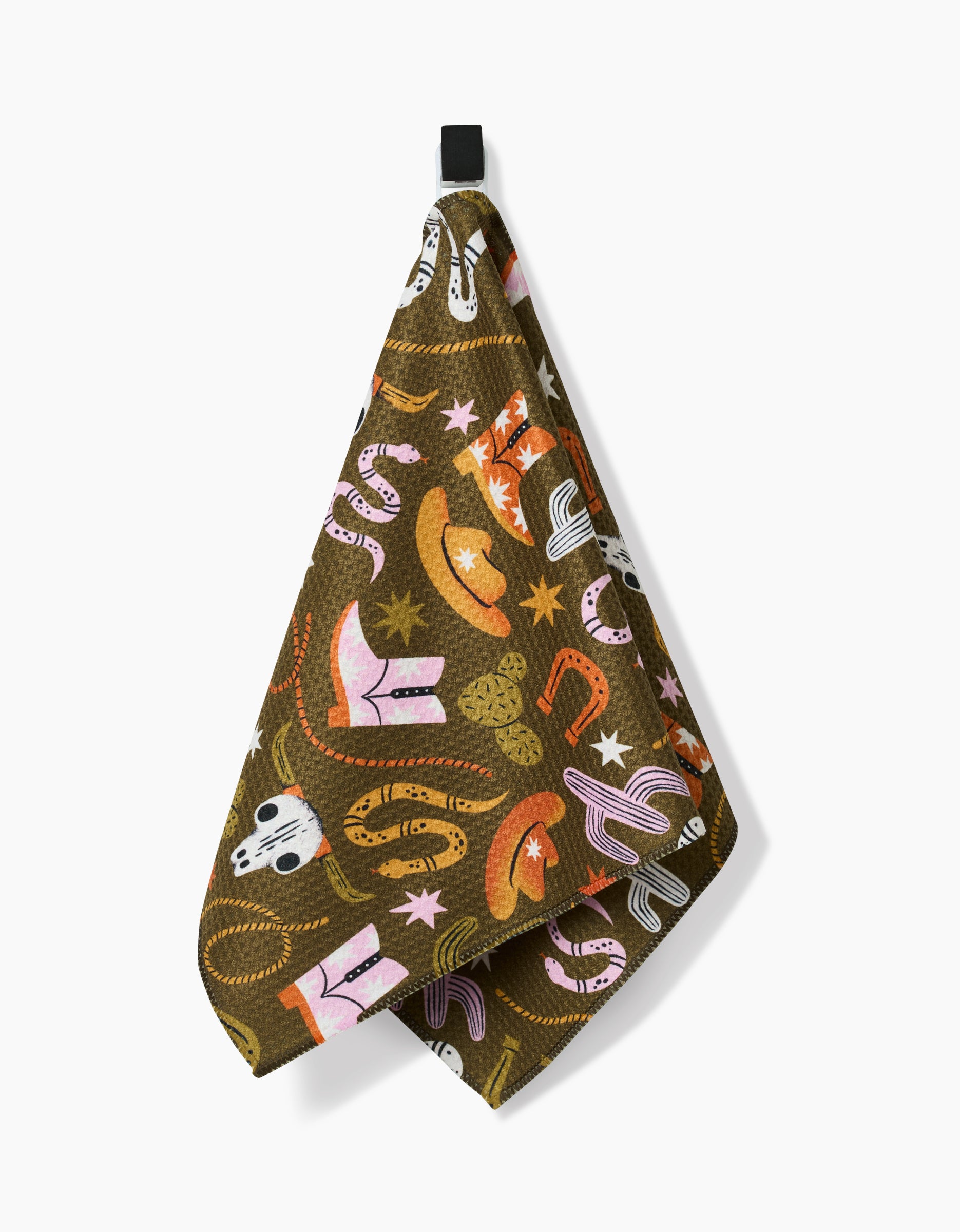 The “Wild Cowboy” bar towel by Megan Roy, made from recycled materials, showcases colorful cowboy-themed illustrations and hangs by a black loop against a white background.