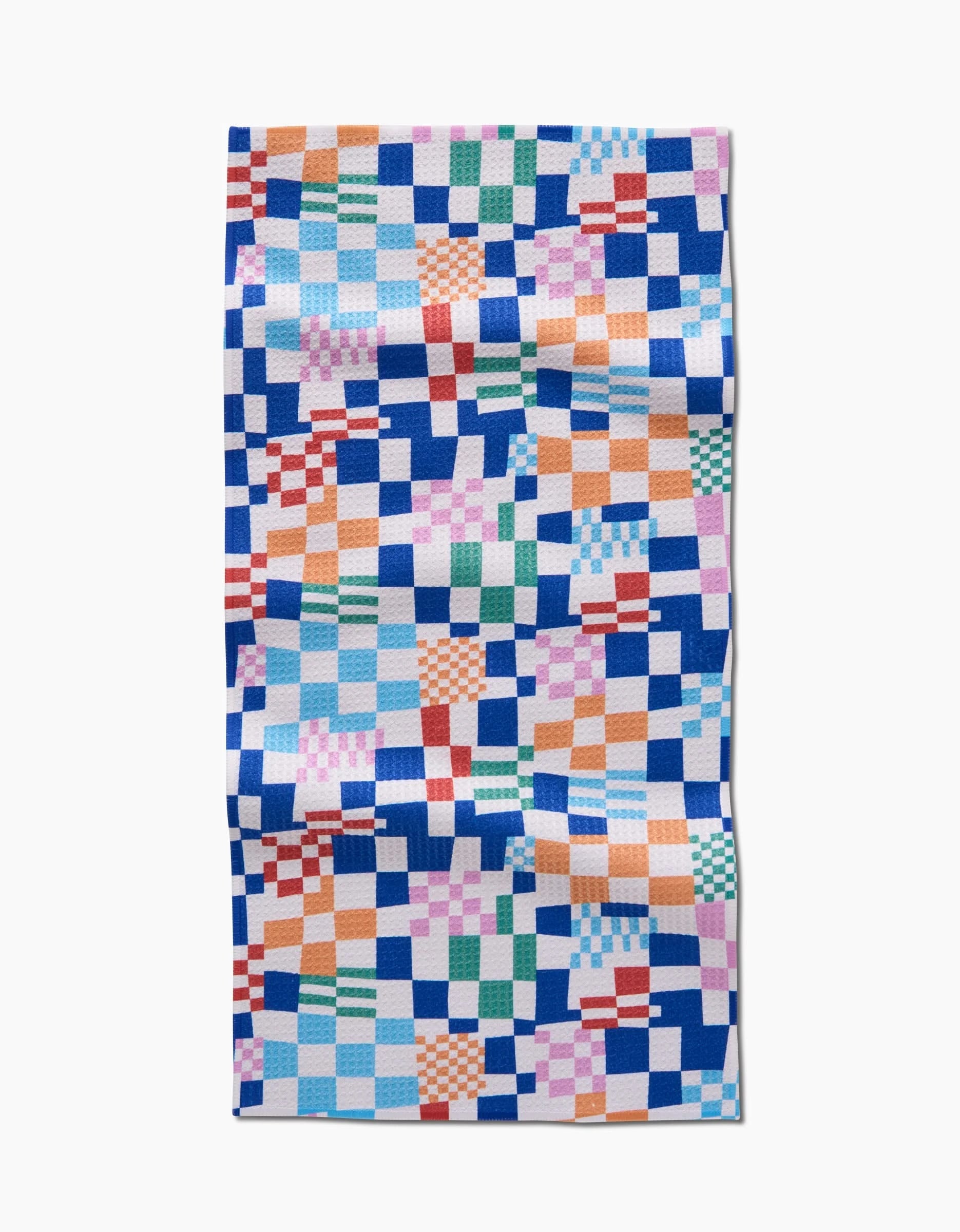 Wonky Checkers by Claire Iglesias is a rectangular Geoweave textile featuring a colorful, irregular checkerboard pattern with blue, pink, orange, green, and white squares. The fabric shows visible creases and is set against a white background.