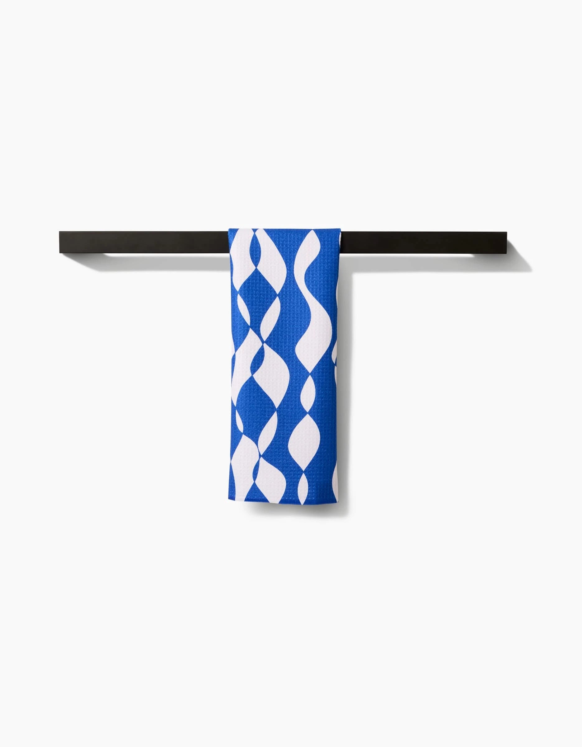 The Wonky Lines bar towel by Claire Iglesias features a blue and white wavy abstract pattern. Made from premium Geoweave fabric, its draped over a black towel bar and combines modern style with superior absorbency.
