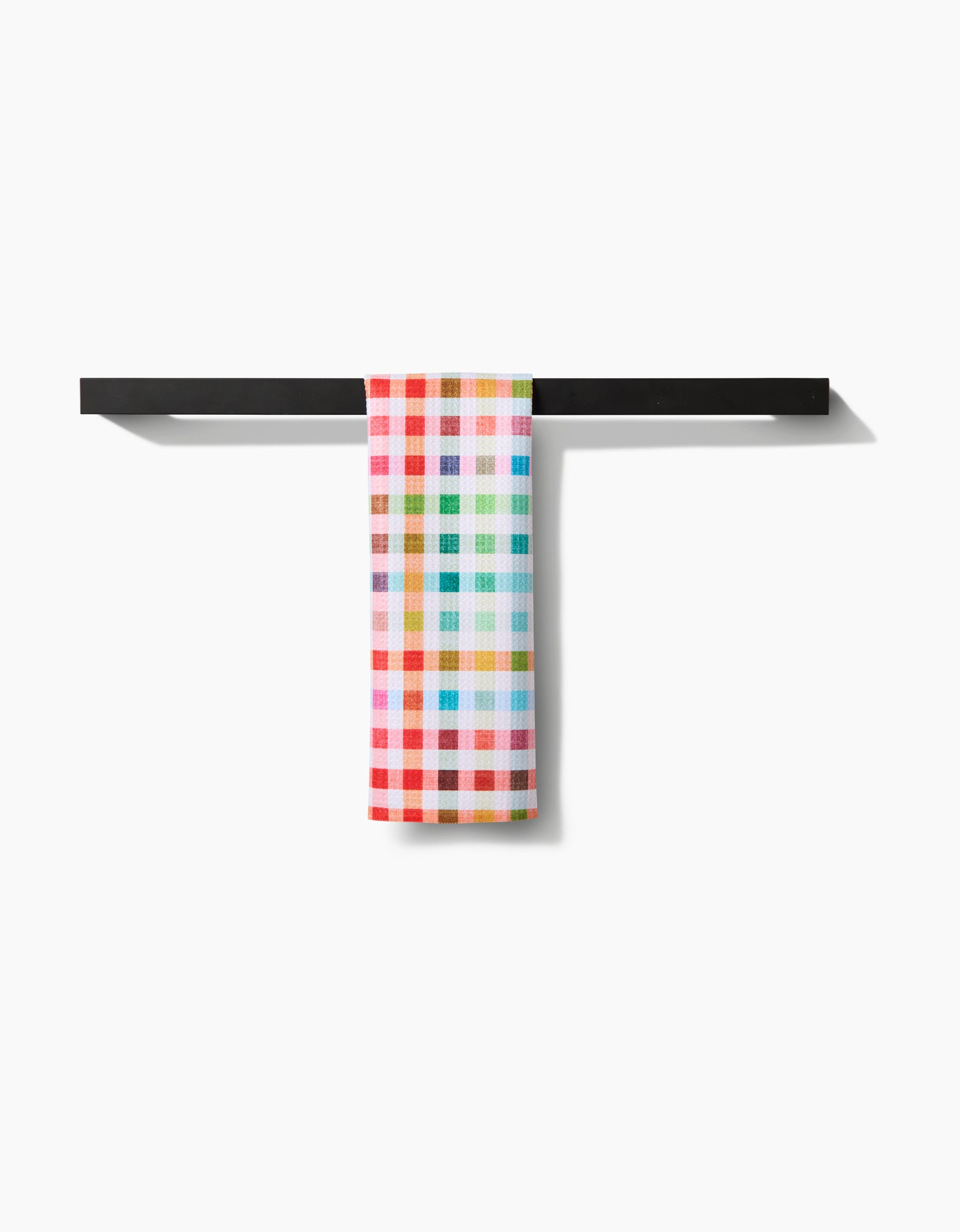 The Pascale Dilger Woven Spring Plaid towel, crafted from recycled materials, hangs neatly on a sleek black horizontal rack against a clean white background.