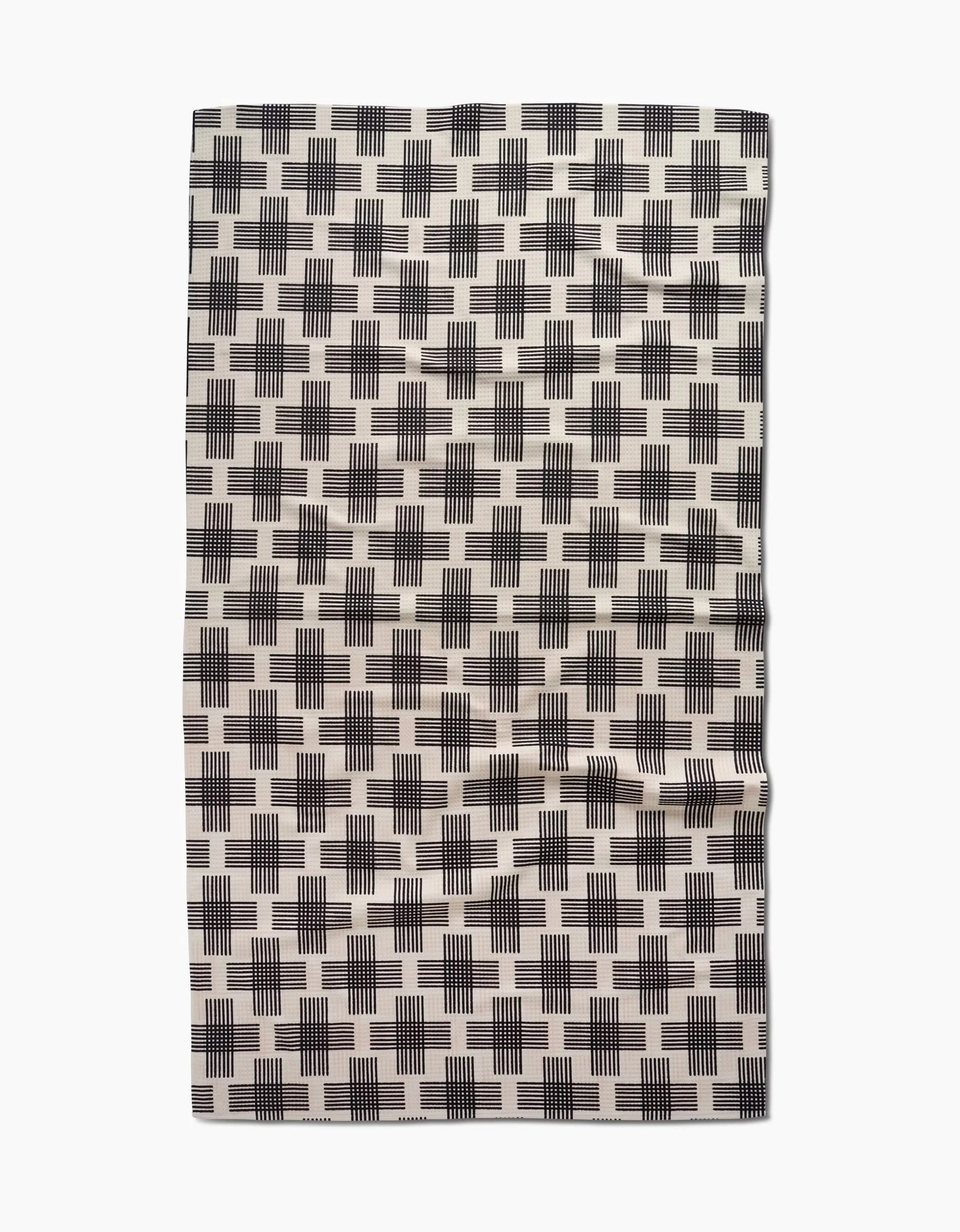 The Cross Hatch Luxe Bath Towel by Rosa Kichline features a cream base with black plus-sign patterns and a slightly wrinkled appearance, crafted using advanced Geoweave technology.
