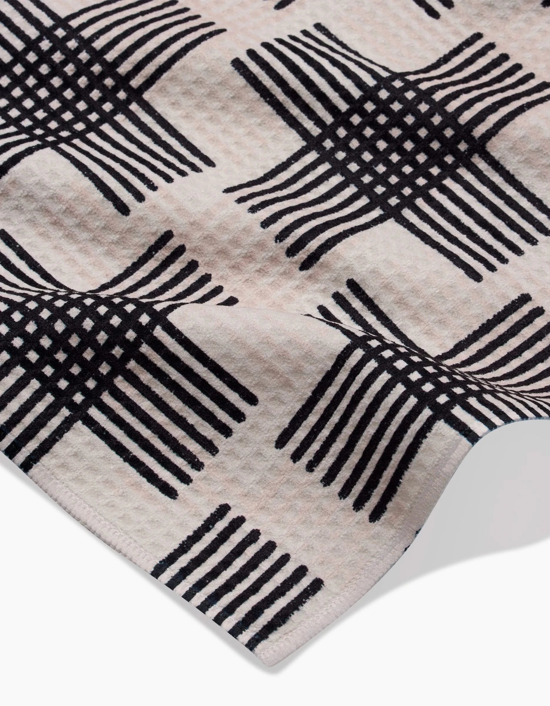 A close-up of Rosa Kichline’s Cross Hatch towel shows its ultra-absorbent Geoweave fabric and raised corner, featuring a repeating black geometric pattern of interlocking lines on a light background.