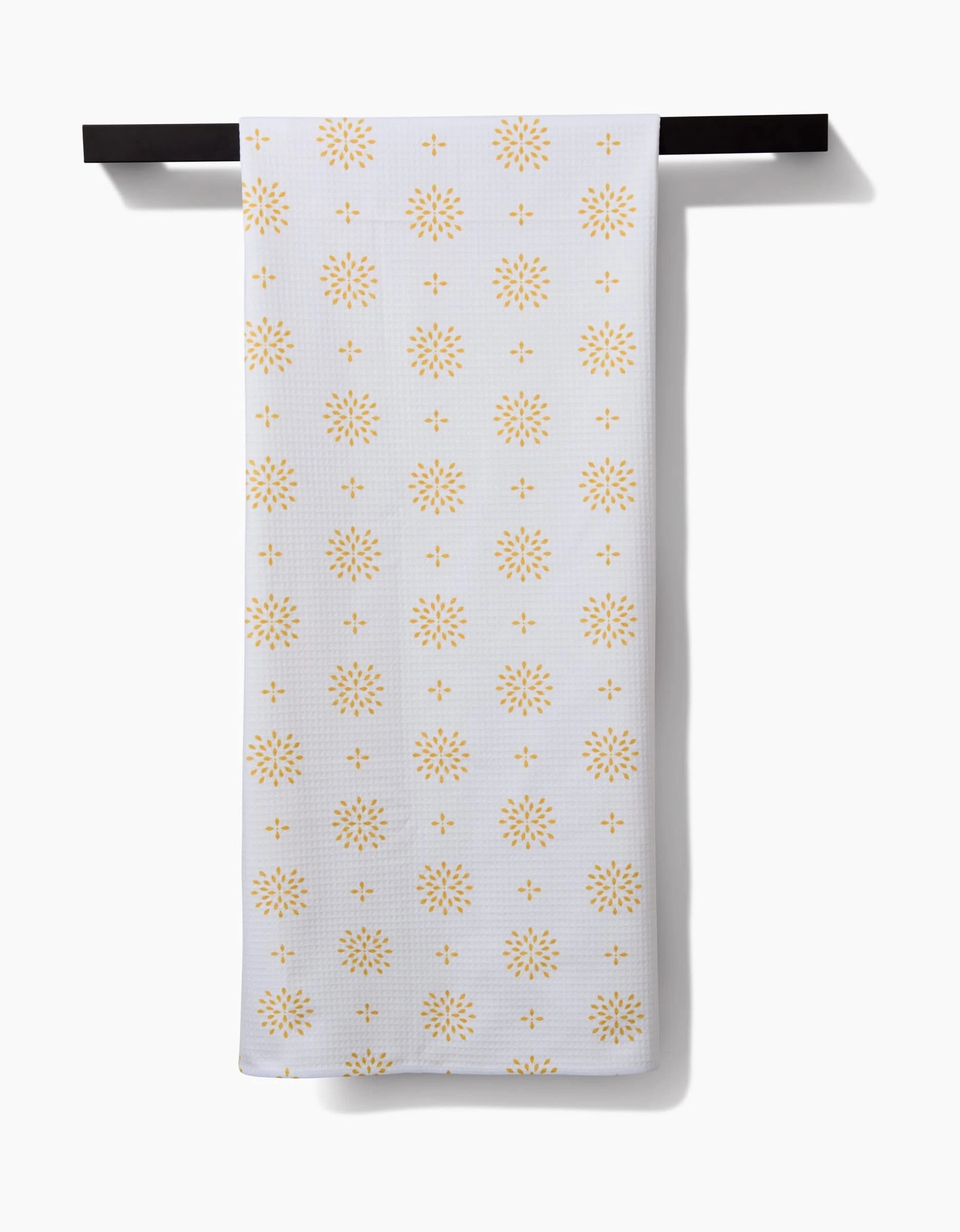 The Danelys Sidron Morning Petals bath towel, featuring a repeating yellow sunburst pattern and Geoweave technology for superior absorbency, hangs neatly on a black towel bar against a plain white background.