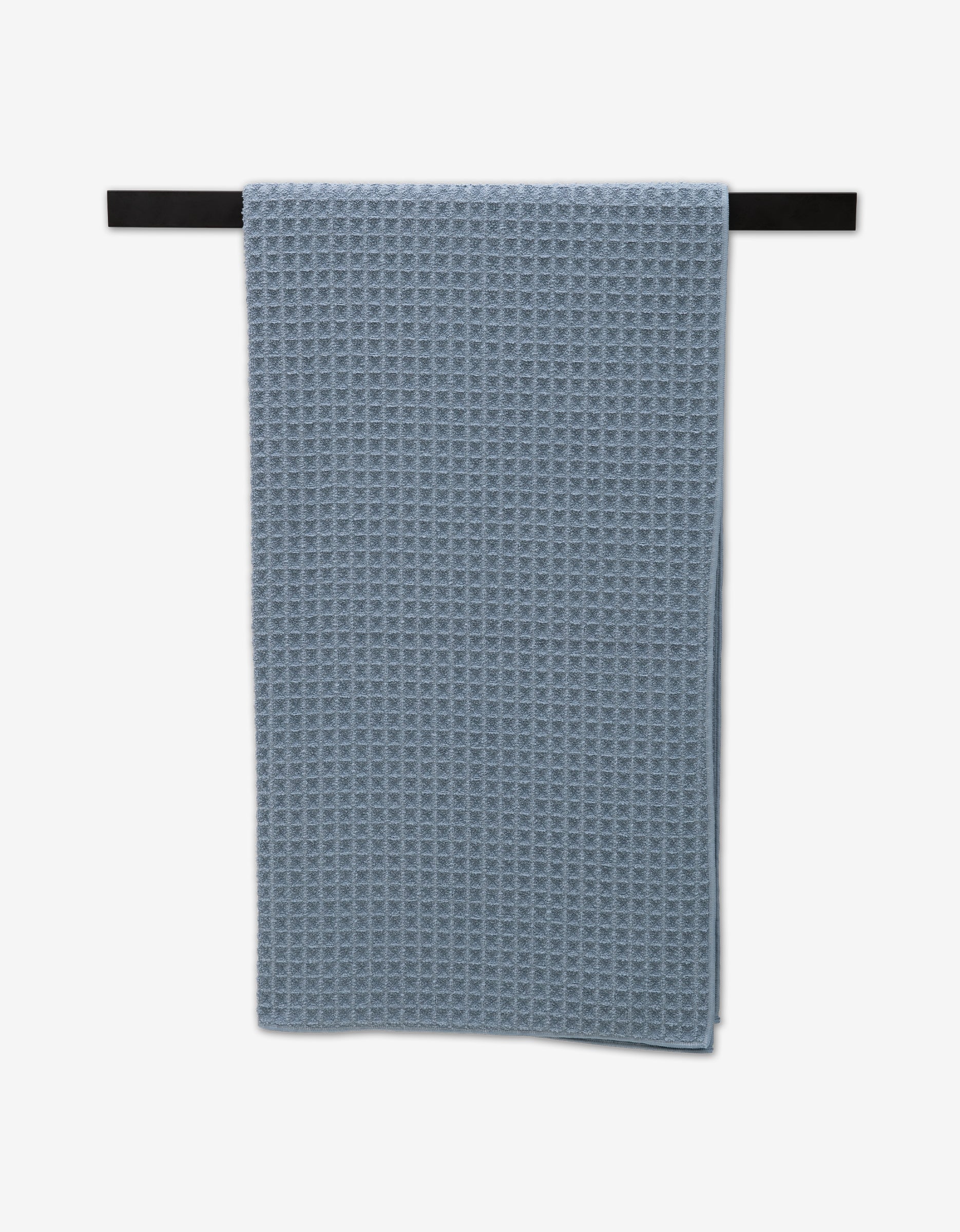 A Sky Bath Towel from GEOMETRY in blue hangs neatly on a black towel bar against a white background, highlighting its ultra-absorbent texture and luxurious appeal.