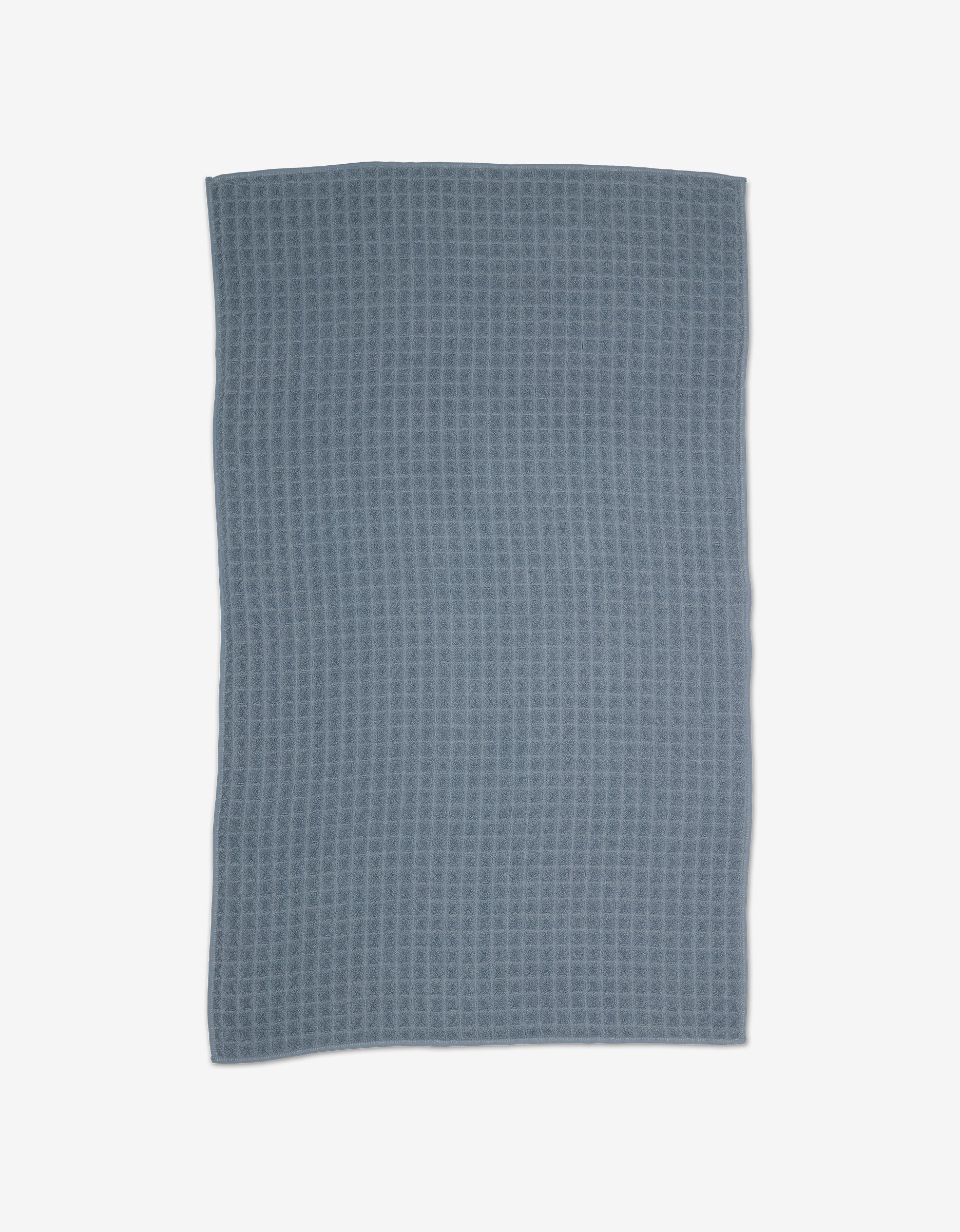 A rectangular, textured GEOMETRY Sky Waffle Bath Towel in blue-gray is laid flat on a light background, highlighting its ultra-absorbent quality.