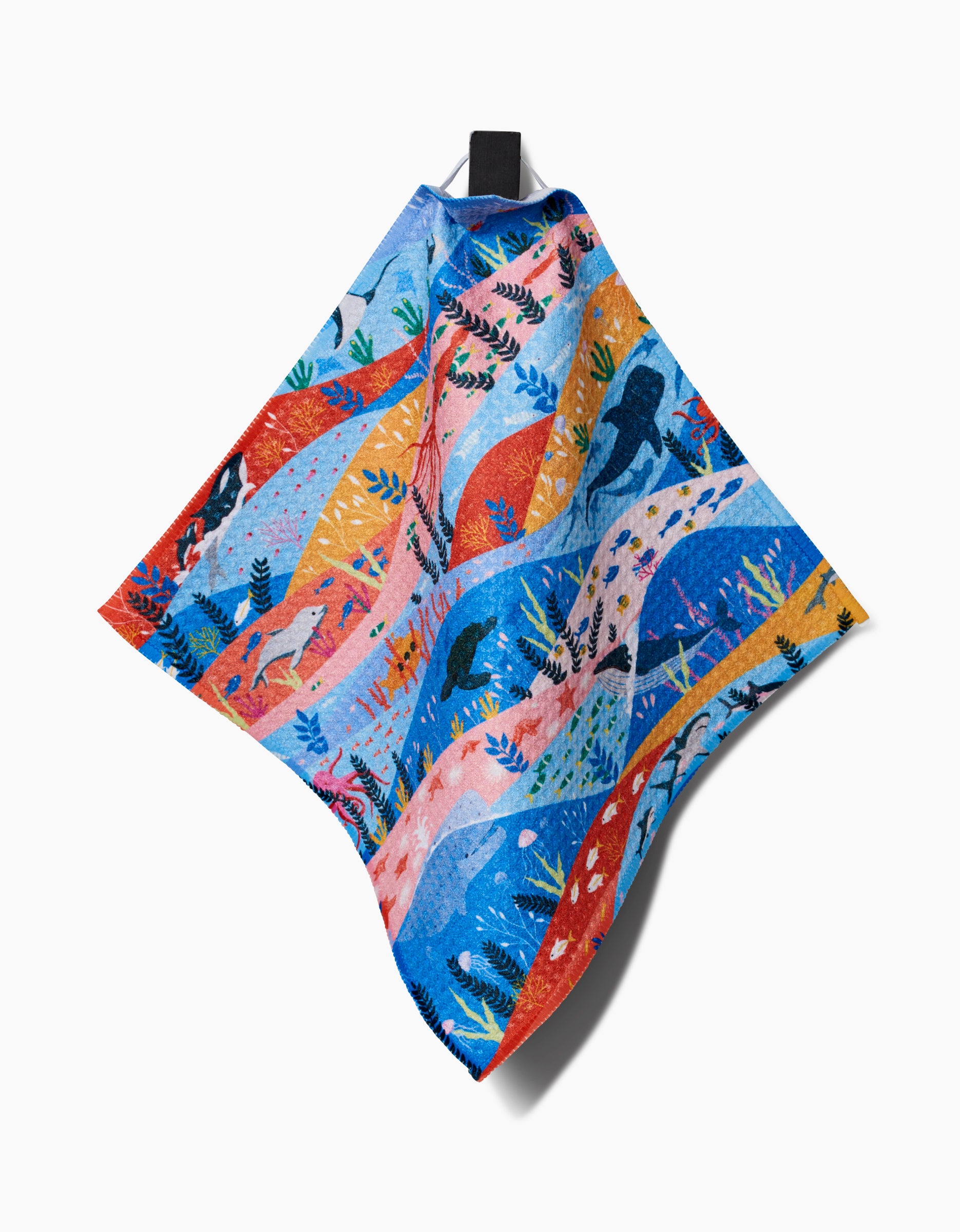The Ceyda Alasar Oceans dishcloth features a vibrant nature-inspired pattern with birds, leaves, and abstract shapes in blue, red, yellow, and pink Geoweave fabric, shown hanging from a black hook on a white background.