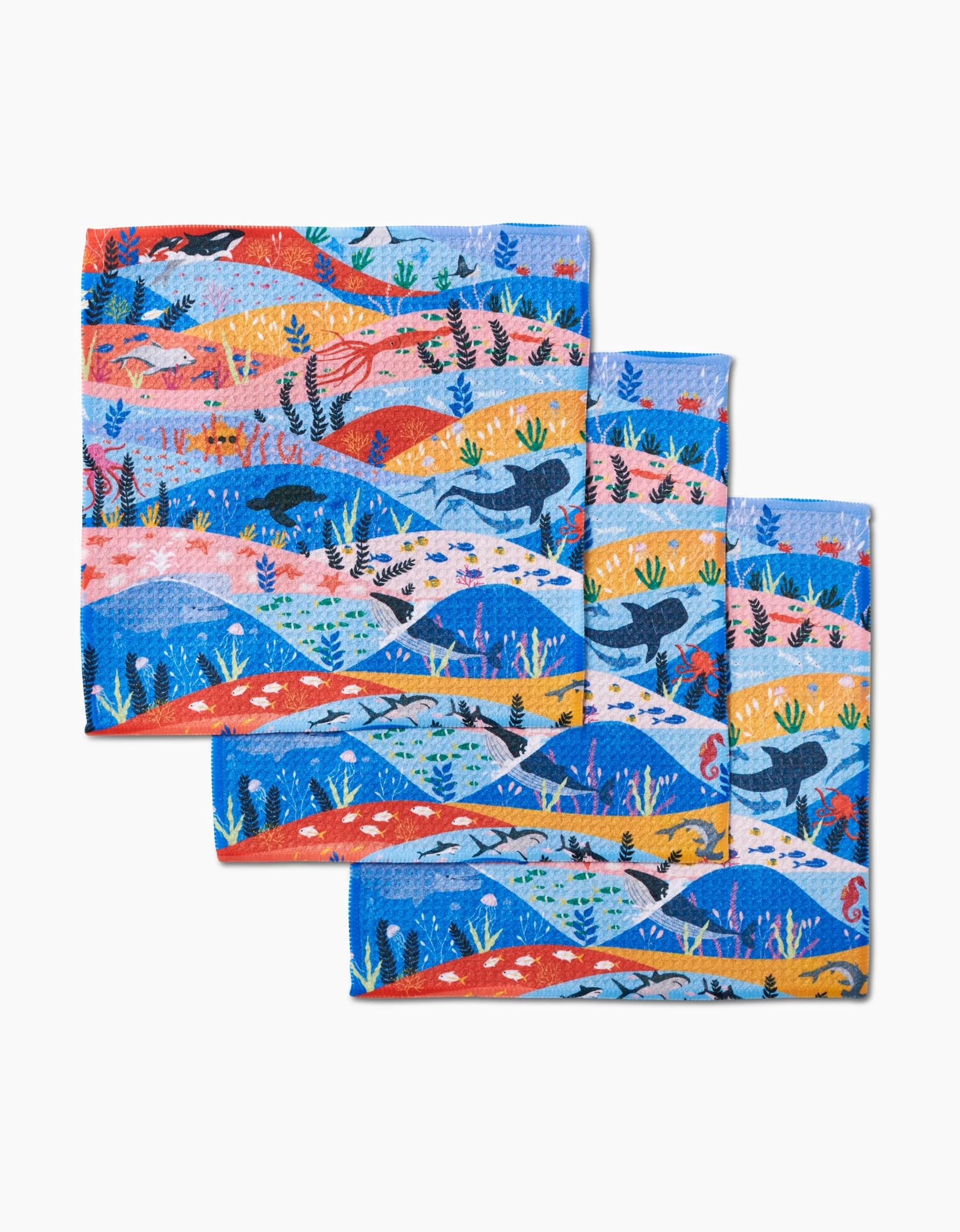 The Oceans dishcloth set by Ceyda Alasar includes three reusable, colorful cloths made from recycled materials featuring whales, fish, seaweed, and coral in vibrant hues on a white background.