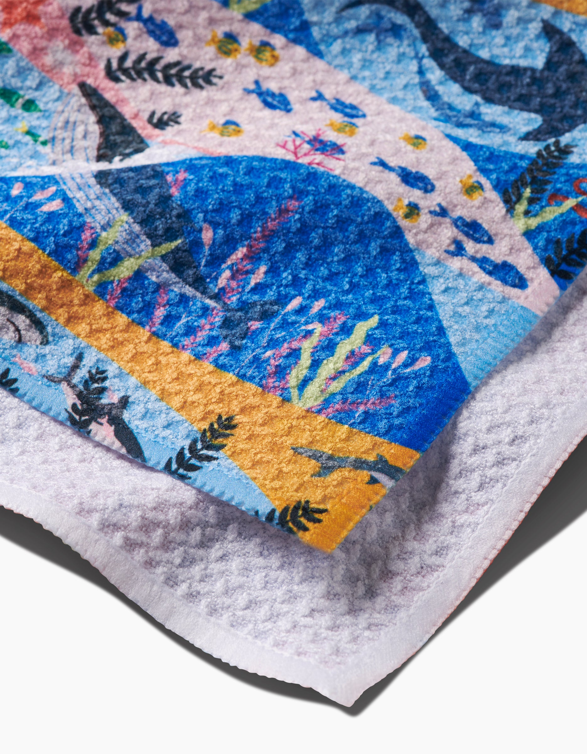 A close-up of the Oceans dishcloth by Ceyda Alasar, showing its colorful underwater scene with fish, whales, and coral in blue, yellow, pink, and orange on soft Geoweave fabric with a gentle dimpled texture.