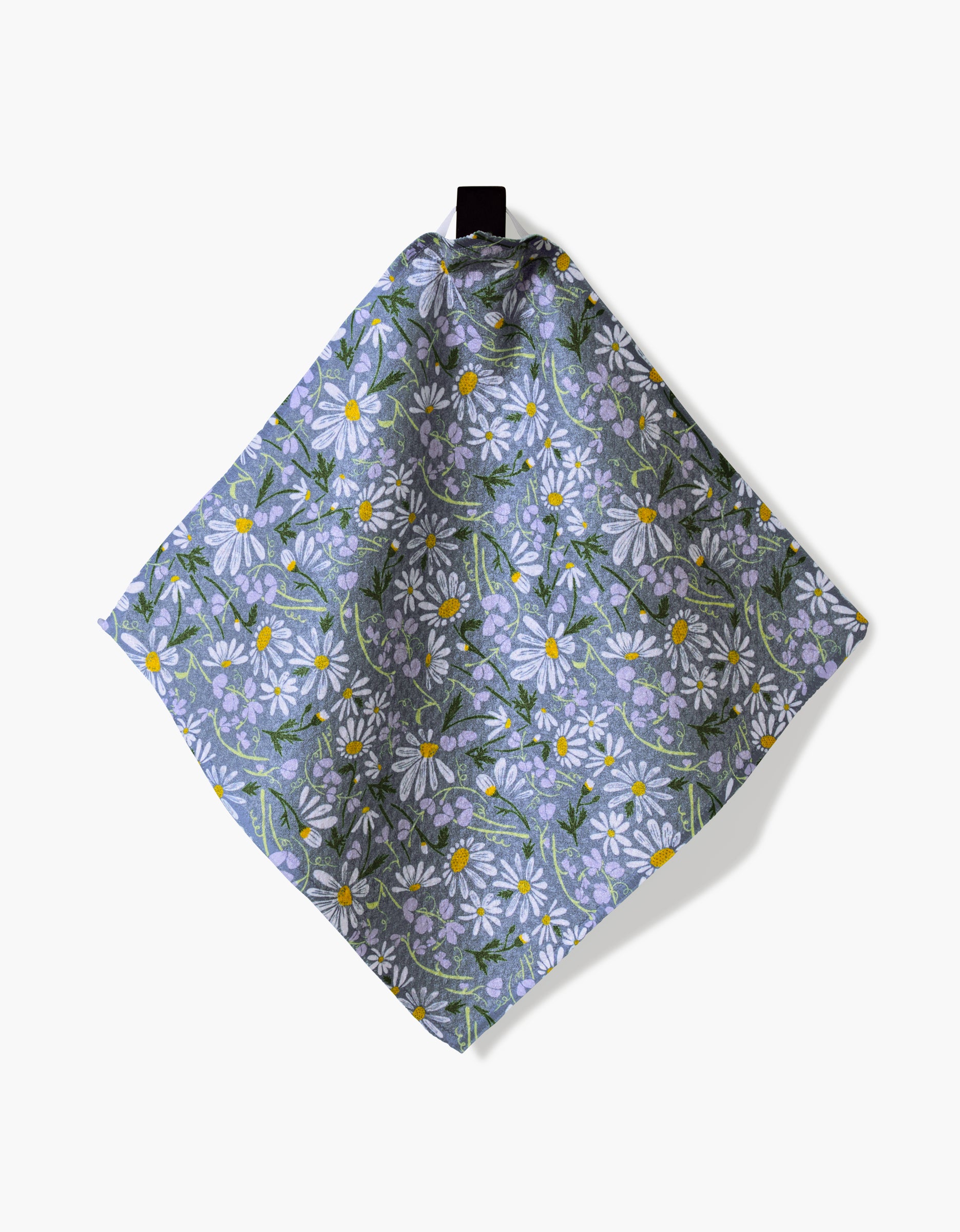April by Elisabeth Wing is a square, eco-friendly cloth napkin with white daisies, yellow centers, and green leaves on lavender geoweave fabric, displayed hanging from a black loop against a white background.
