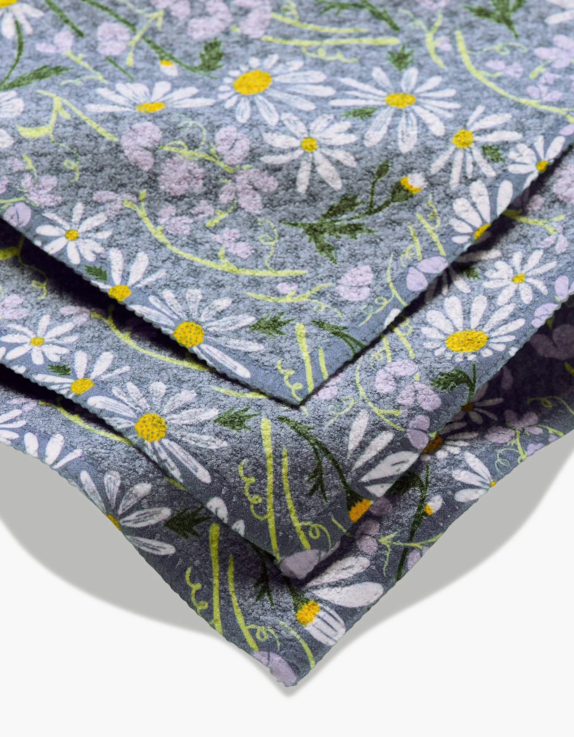 A close-up of Elisabeth Wings April dishcloth, made from eco-friendly Geoweave fabric and featuring a blue background with white daisies, yellow centers, and small purple flowers.