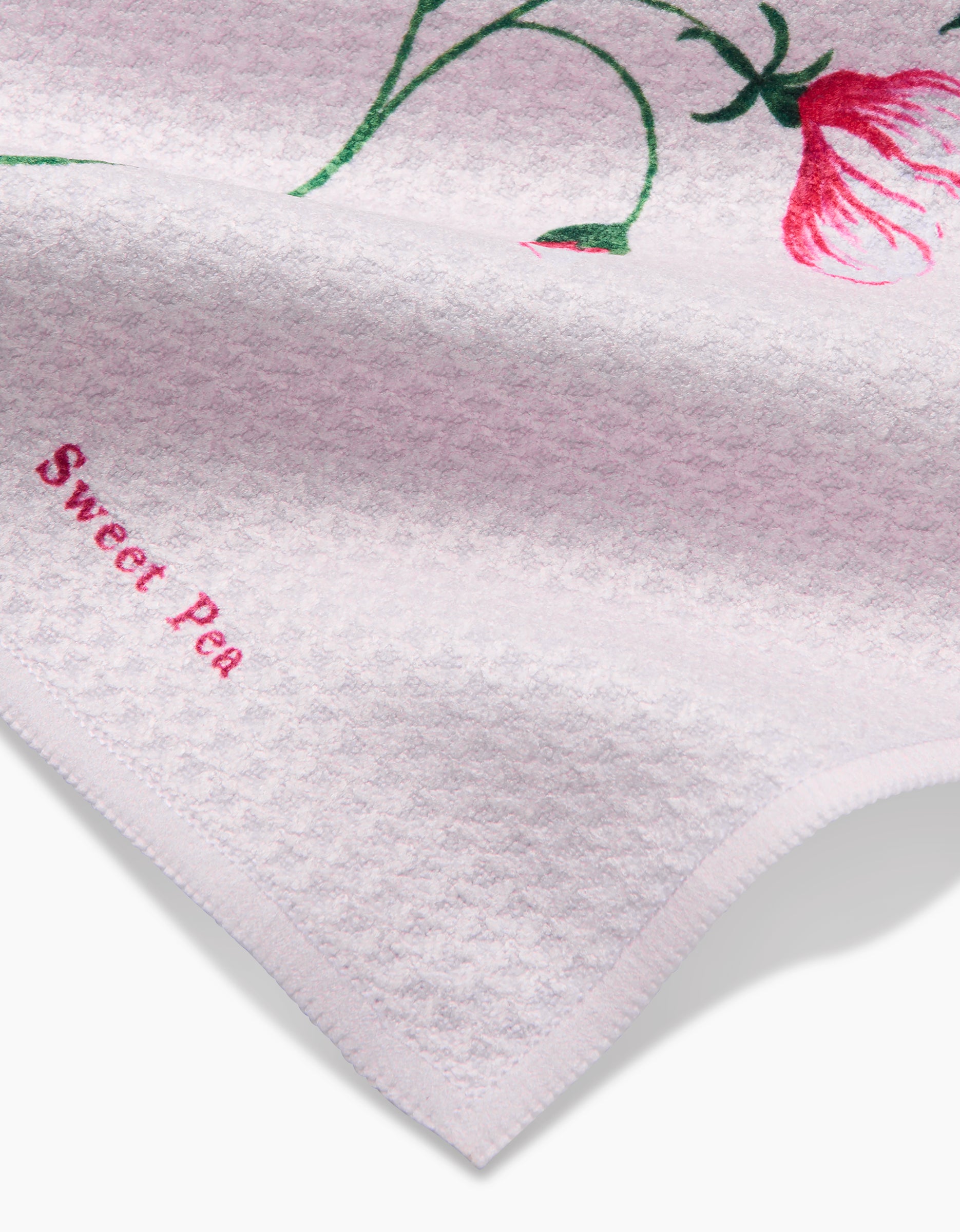 A close-up of the Linda Fox April Sweet Pea Geoweave dishcloth, light pink with a red flower, green stem, and “Sweet Pea” embroidered in pink on the corner.