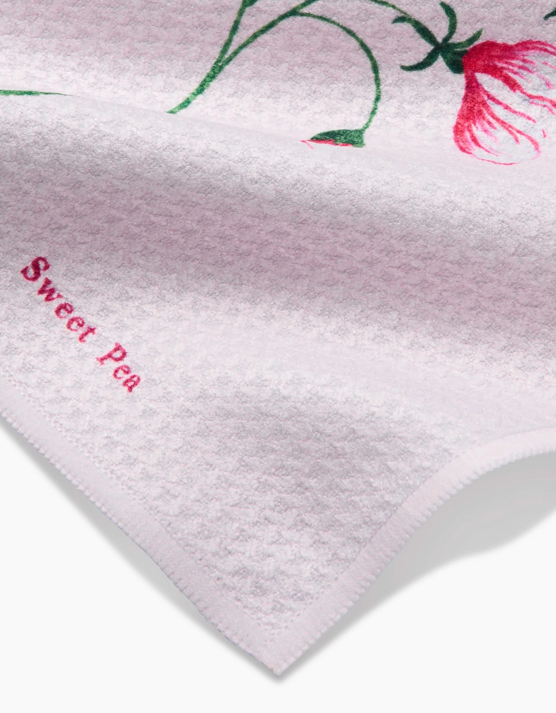 A close-up of the Linda Fox April Sweet Pea Geoweave dishcloth, light pink with a red flower, green stem, and “Sweet Pea” embroidered in pink on the corner.