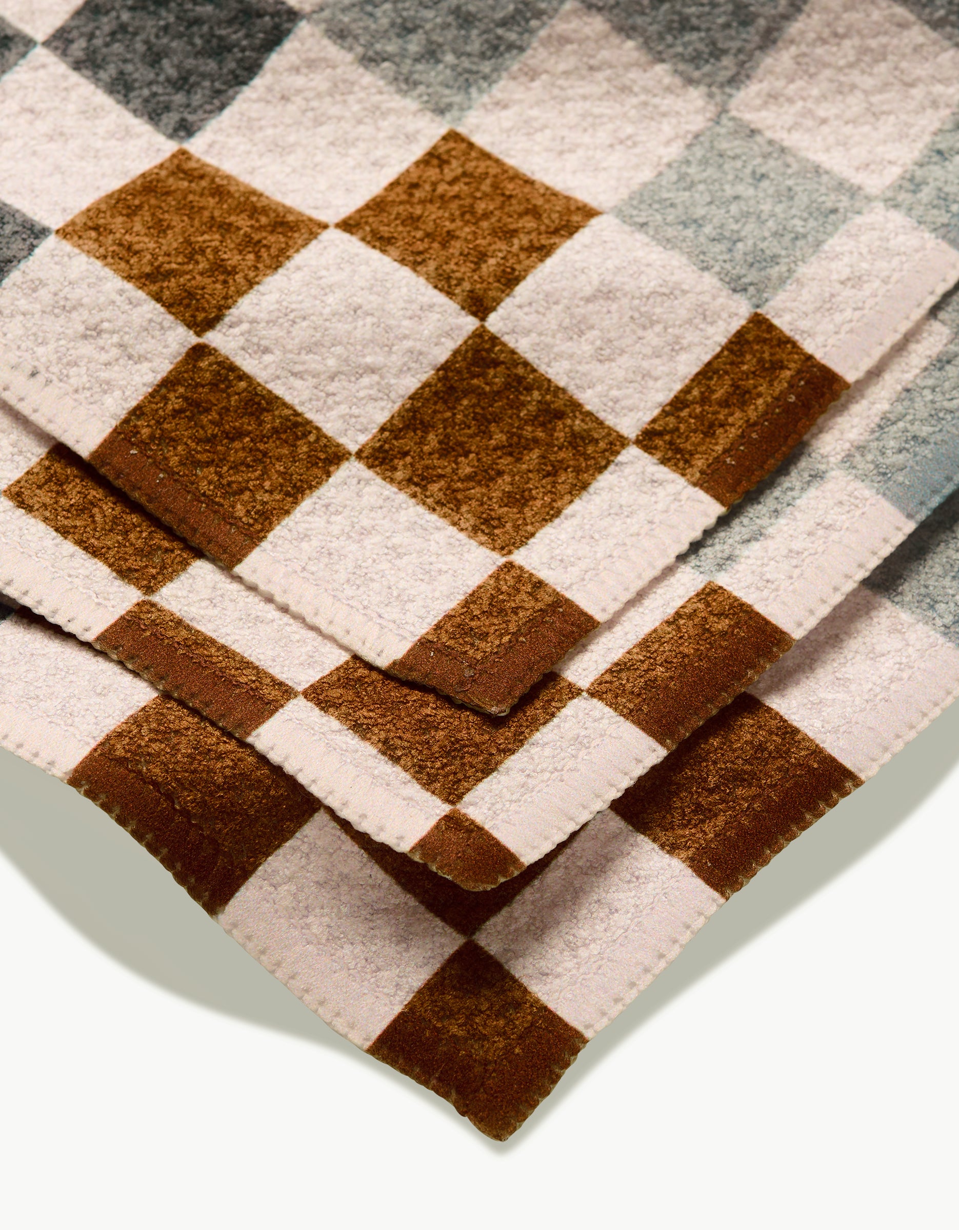 A close-up of two stacked GEOMETRY Autumn Checkers dishcloths, made with Geoweave fabric and featuring brown, beige, and grayish-blue checkered squares on a light background.
