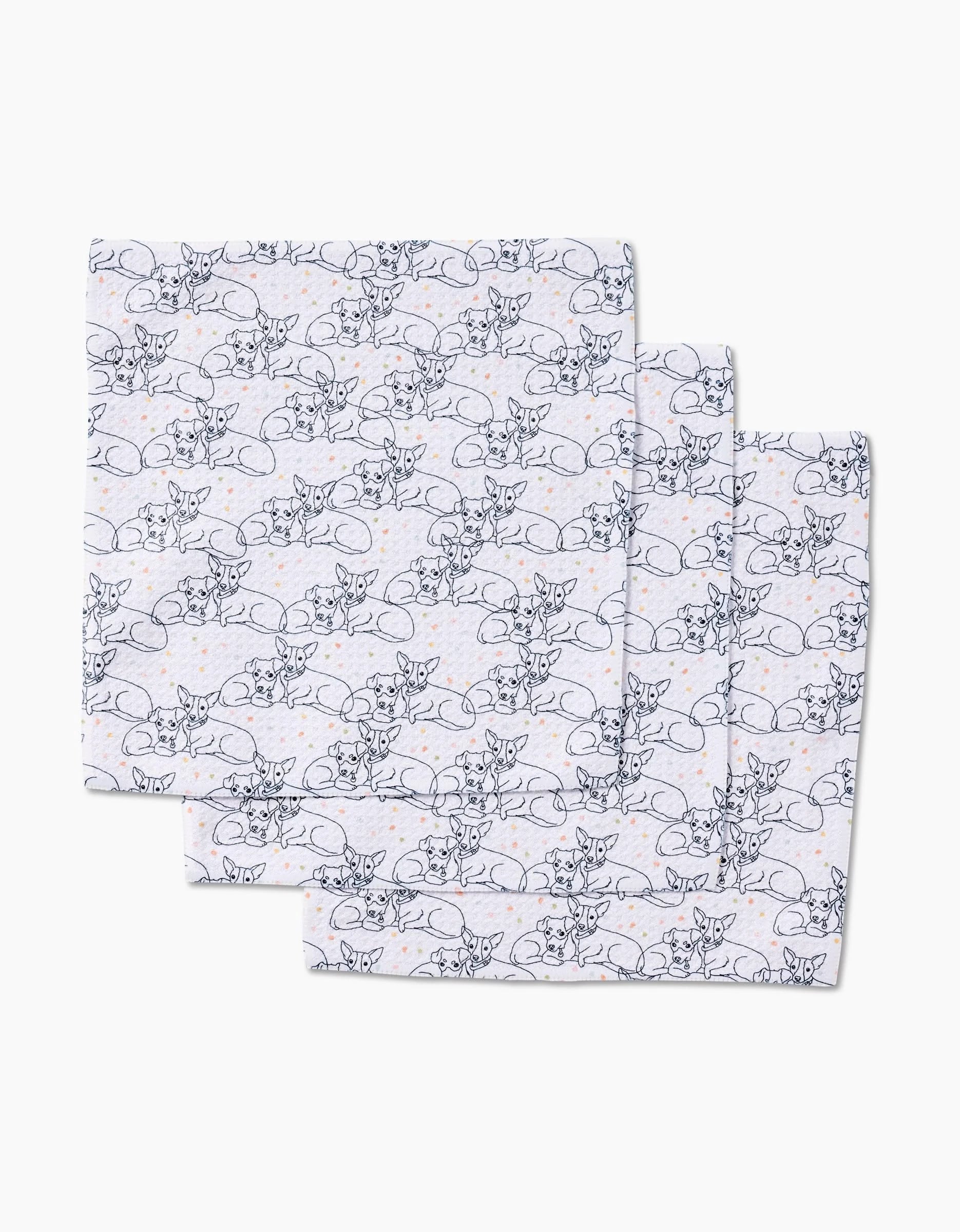 Three white Berry and Louie cloth napkins by Sweet Simple Vegan, featuring a repeating line-art pattern of reclining deer and small orange dots, are neatly stacked with their edges slightly overlapping.