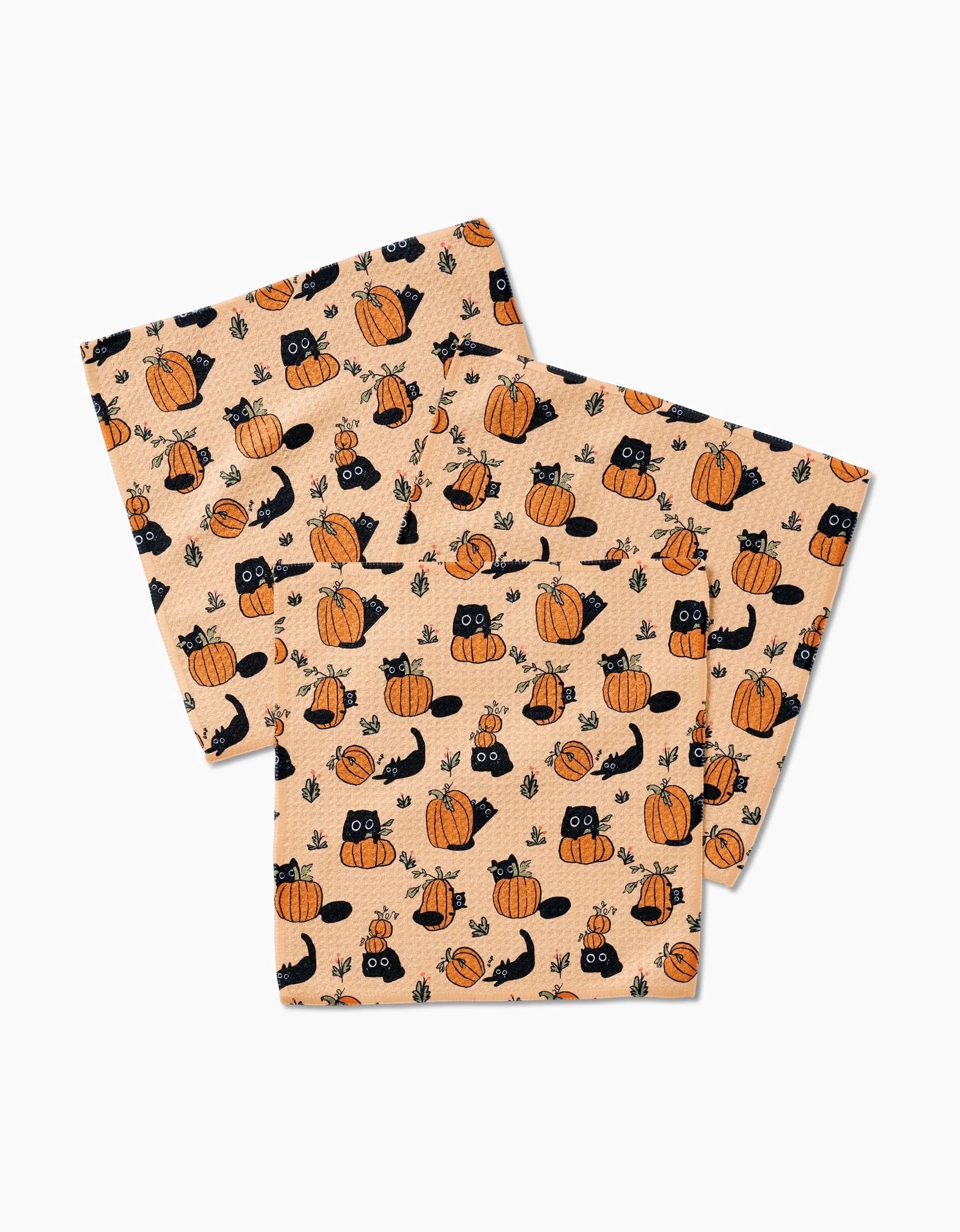Three Janna Sue Design Black Cats Geoweave dishcloths, tan with Halloween patterns of black cats, pumpkins, leaves, and acorns, are layered and slightly overlapping on a white background.