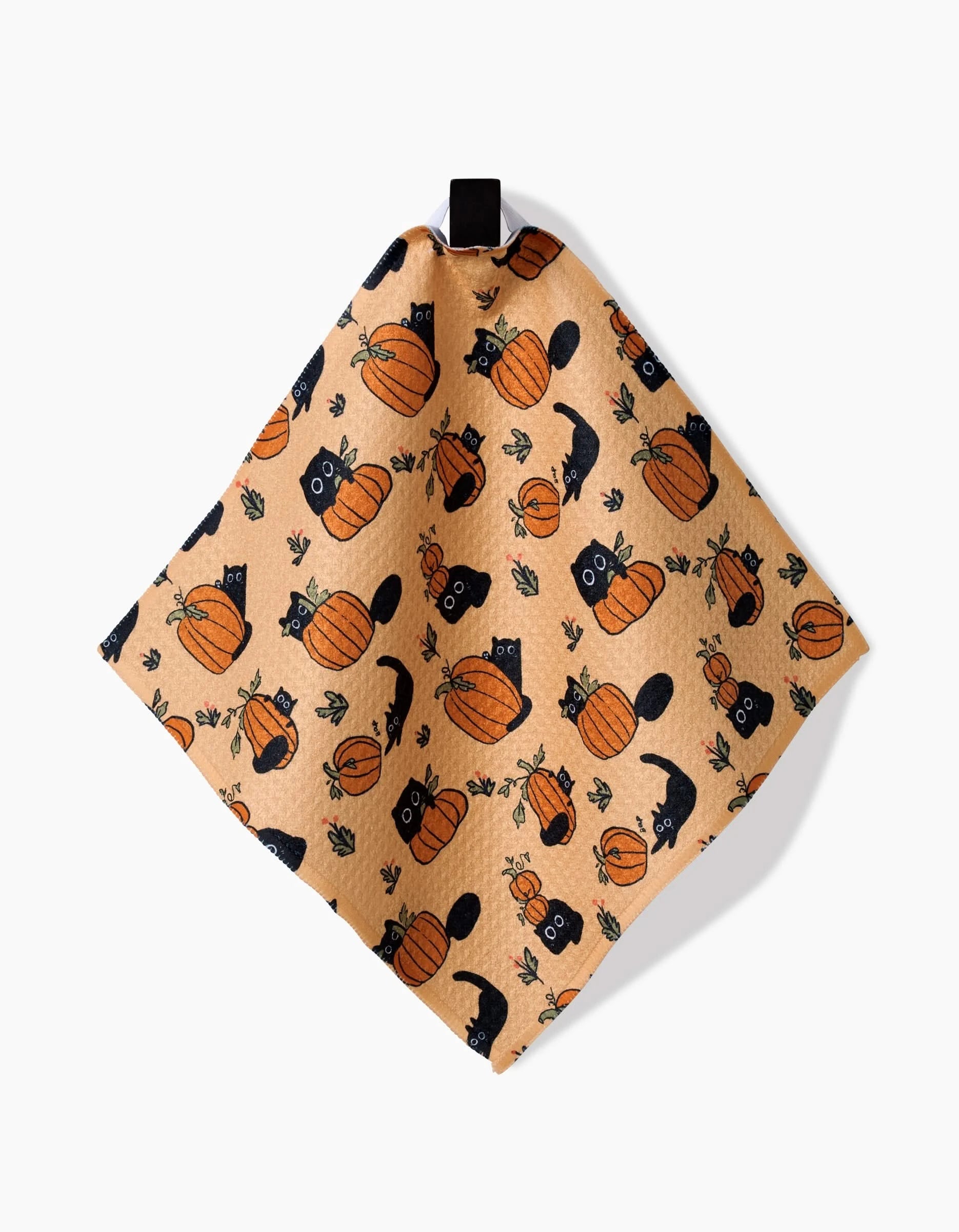 The Black Cats napkin by Janna Sue Design is peach-colored, made from recycled materials, features black cats, pumpkins, and autumn leaves, and includes a black hanging loop at the top.
