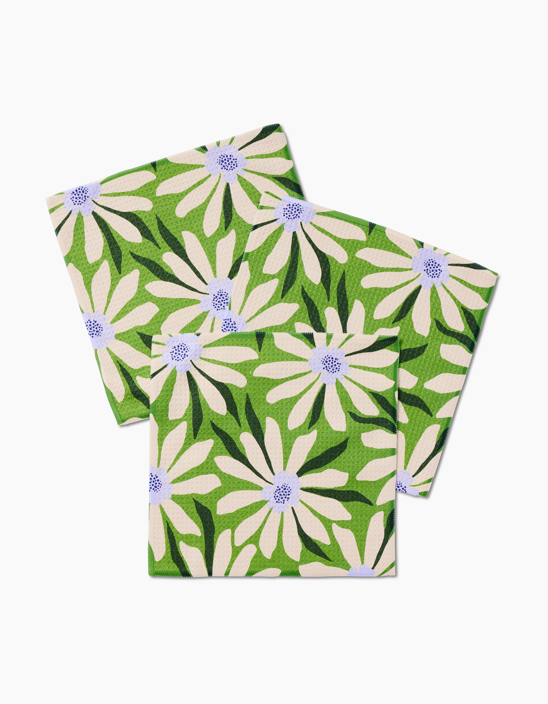 Bliss and Bloom by GEOMETRY: Two folded cloth napkins made from recycled materials, featuring a green background with white daisies, purple centers, and dark green leaves.