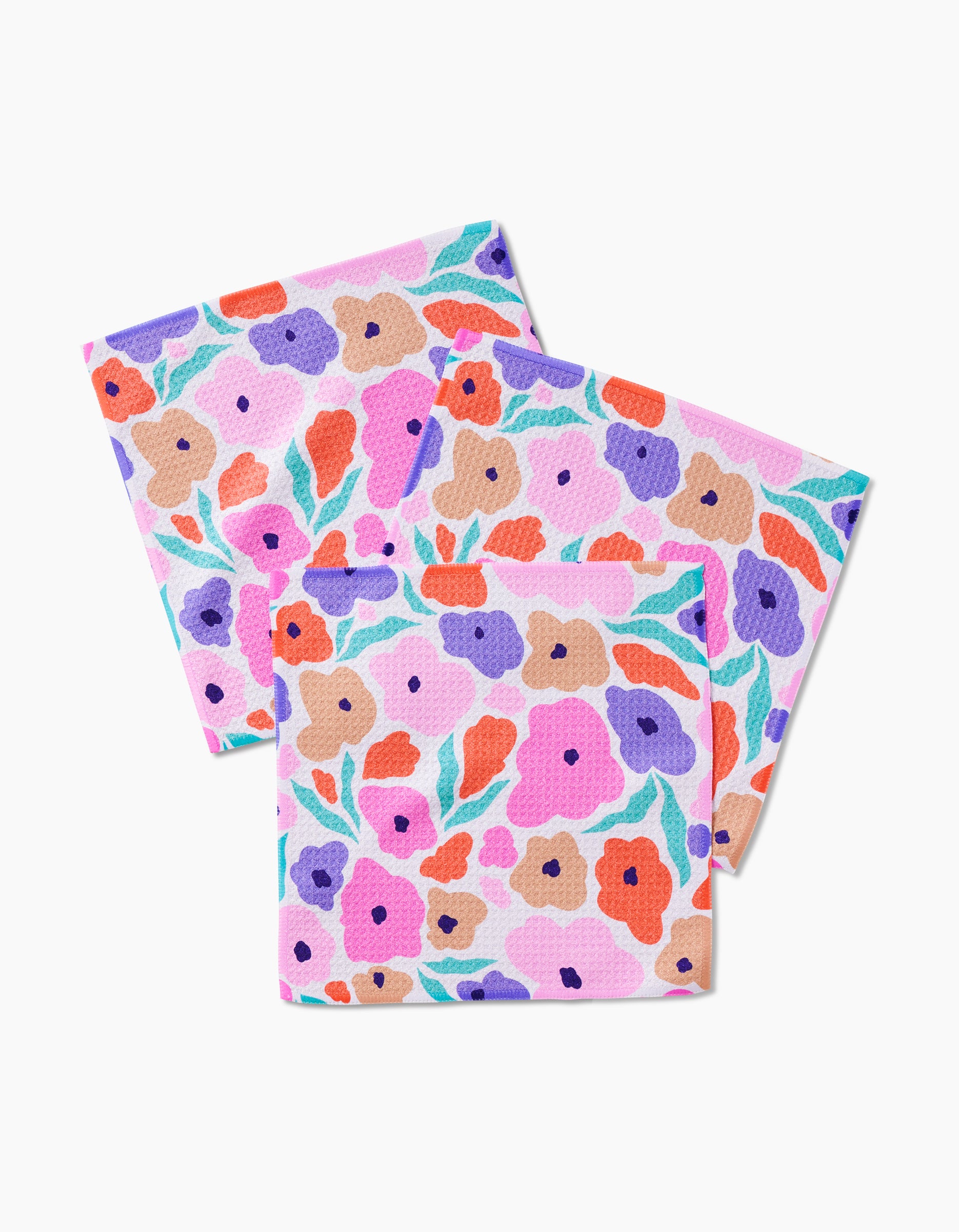 Three GEOMETRY Blossoming Love dishcloths—with colorful floral patterns in pink, purple, red, orange, and green—made from recycled materials are arranged overlapping on a white background.