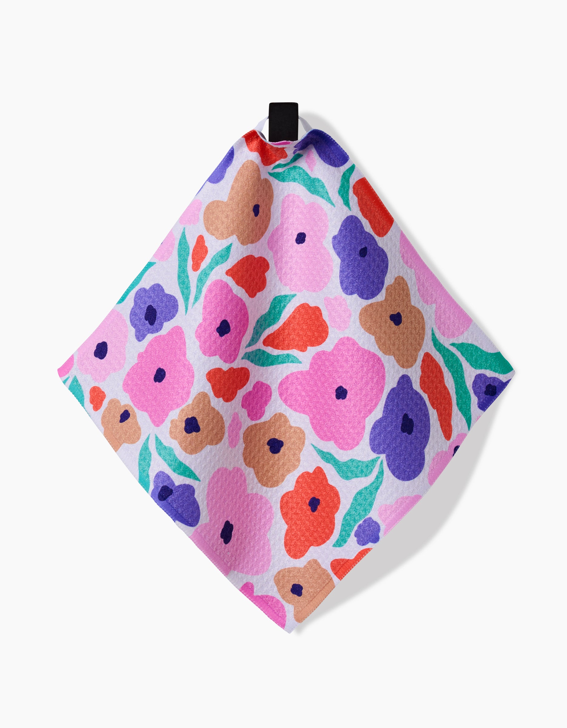 The GEOMETRY Blossoming Love dishcloth is square, made from recycled materials, and features a vibrant floral pattern in pink, red, purple, blue, and tan on light pink, with a black hanging loop at the top.