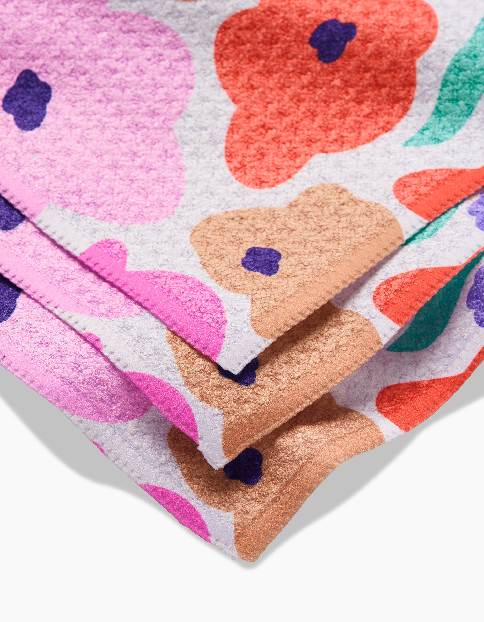 A close-up of the GEOMETRY Blossoming Love Geoweave dishcloth, folded to reveal its vibrant pink, orange, tan, and purple floral pattern on white—crafted from recycled materials.