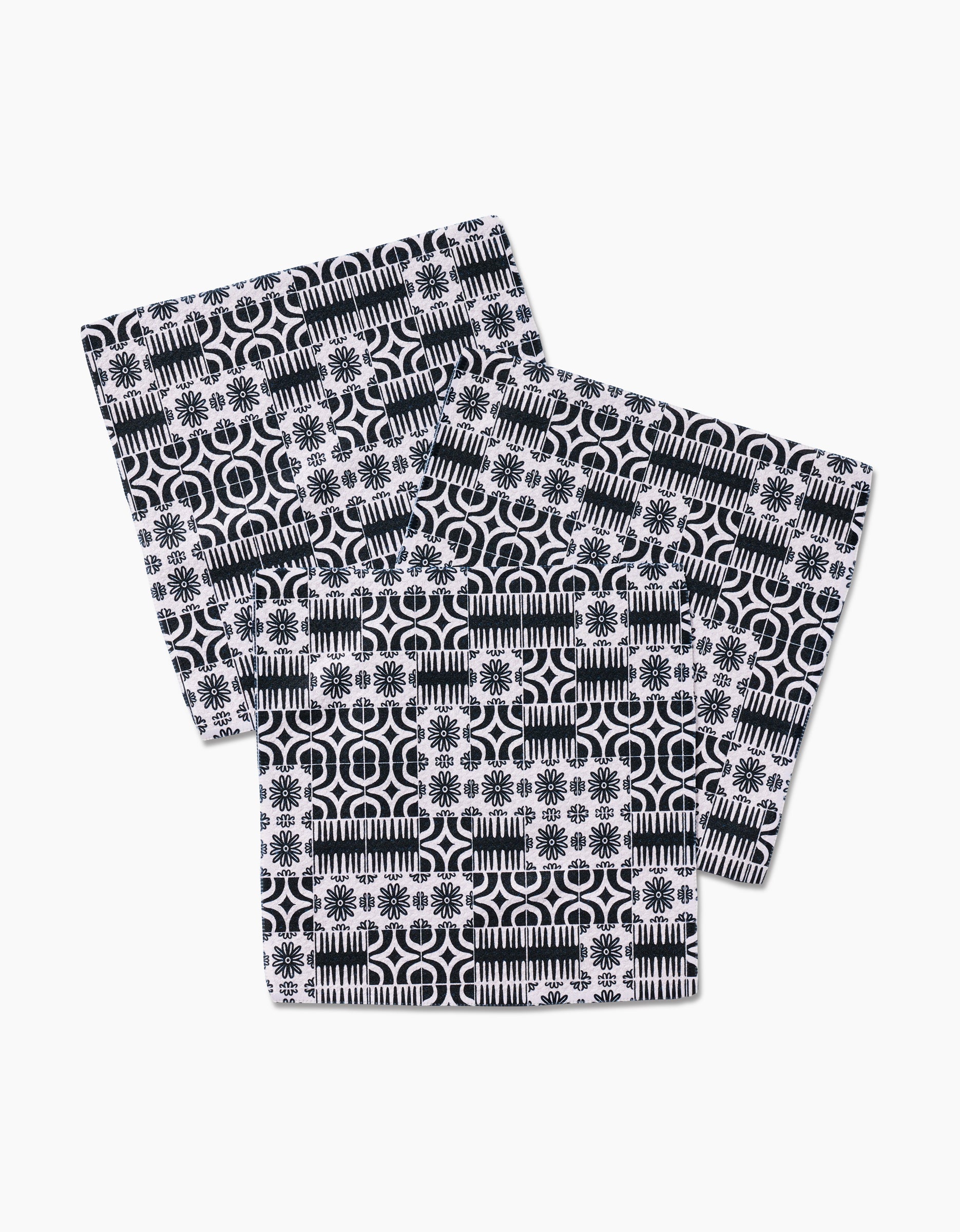 Three Bohemian Mosaic napkins by GEOMETRY, featuring black and white geometric and floral patterns, made from recycled materials, are shown overlapping on a white background.