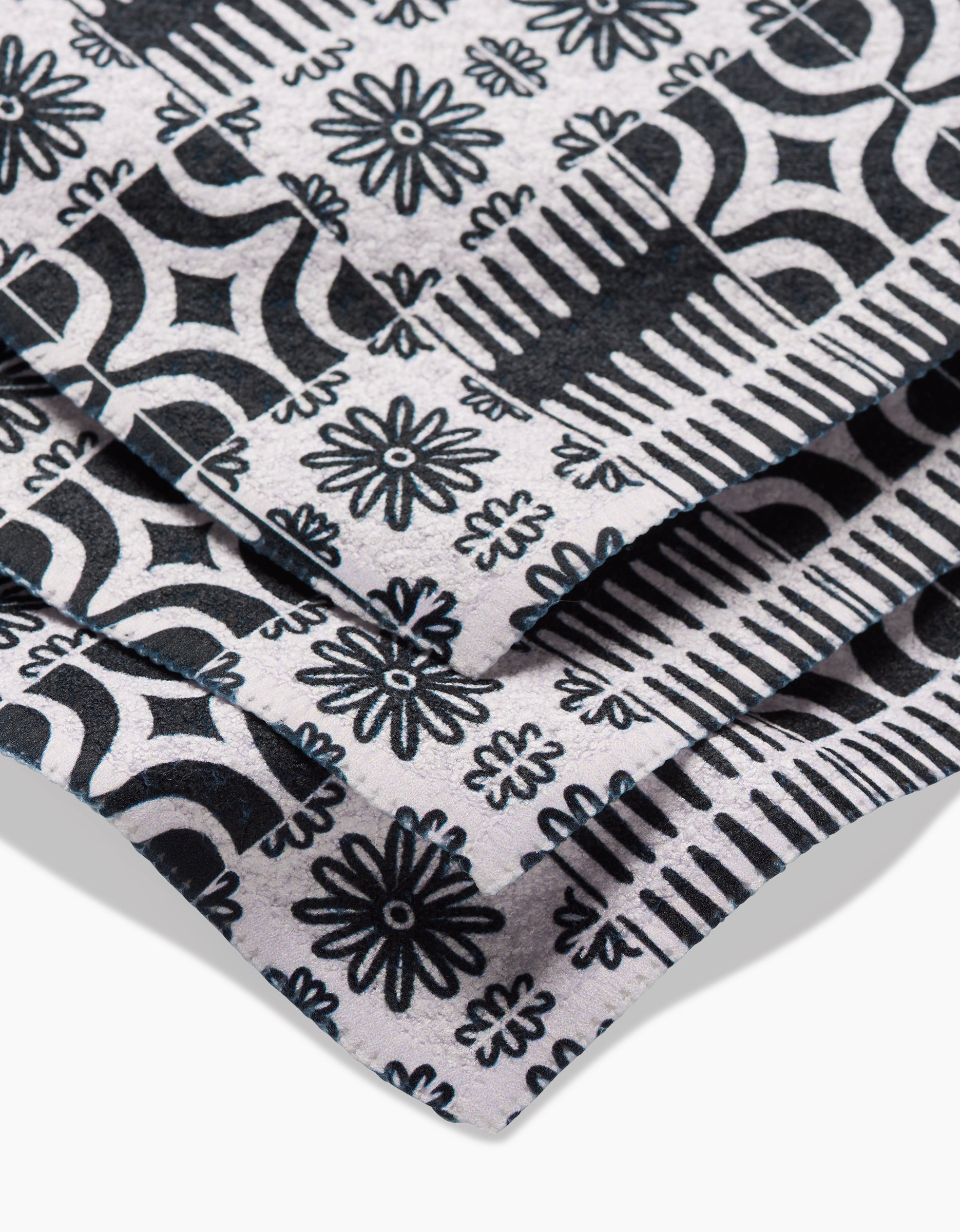 Close-up of GEOMETRYs Bohemian Mosaic dishcloth, made from recycled Geoweave fabric. Features a black and white geometric and floral pattern of repeating flowers, diamonds, and lines on a light background.